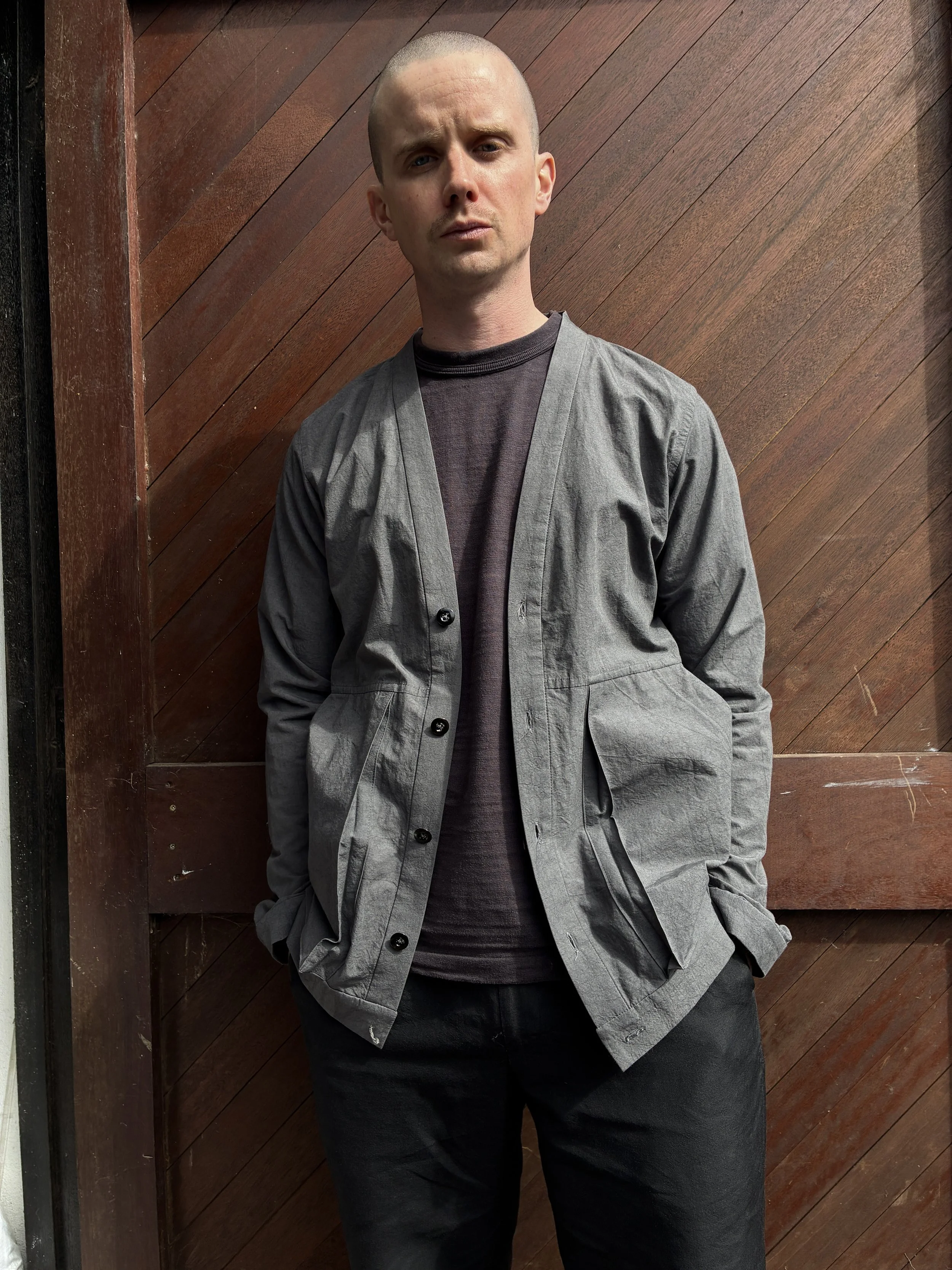 Man in front of wooden door wearing Frank Leder Grey Japanese Cotton Cardigan with hands in pockets