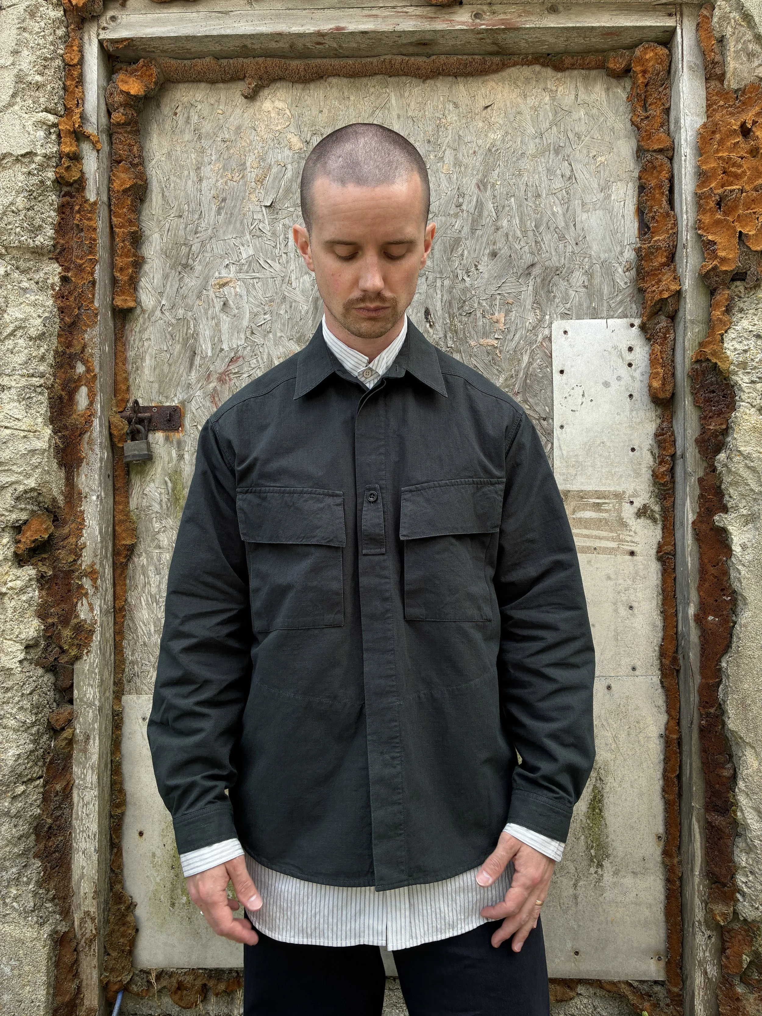 Man in front of wall wearing 1st PAT-RN Sumatra Charcoal Overshirt