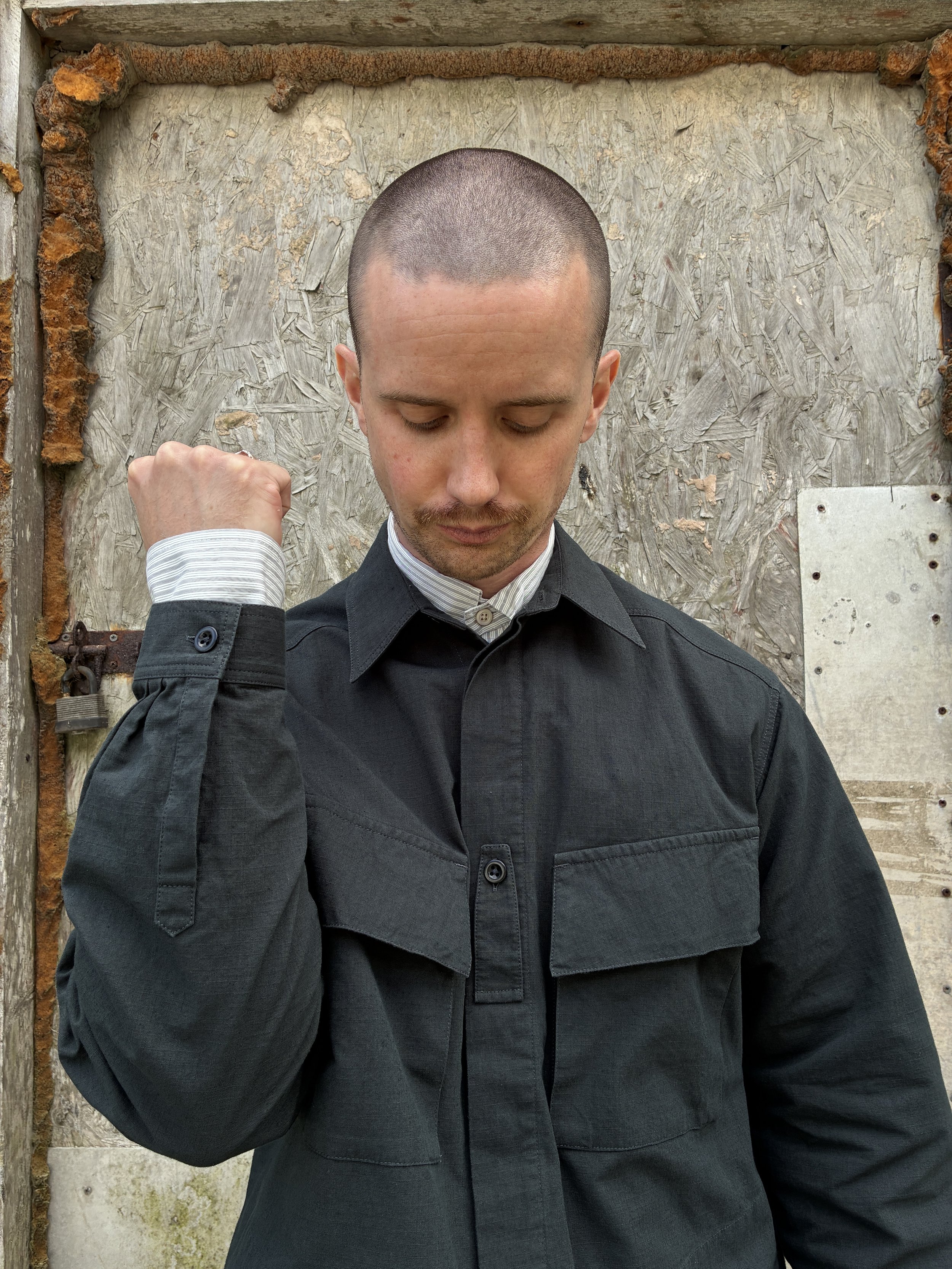 Man in front of wall wearing 1st PAT-RN Sumatra Charcoal Overshirt holding up the cuff