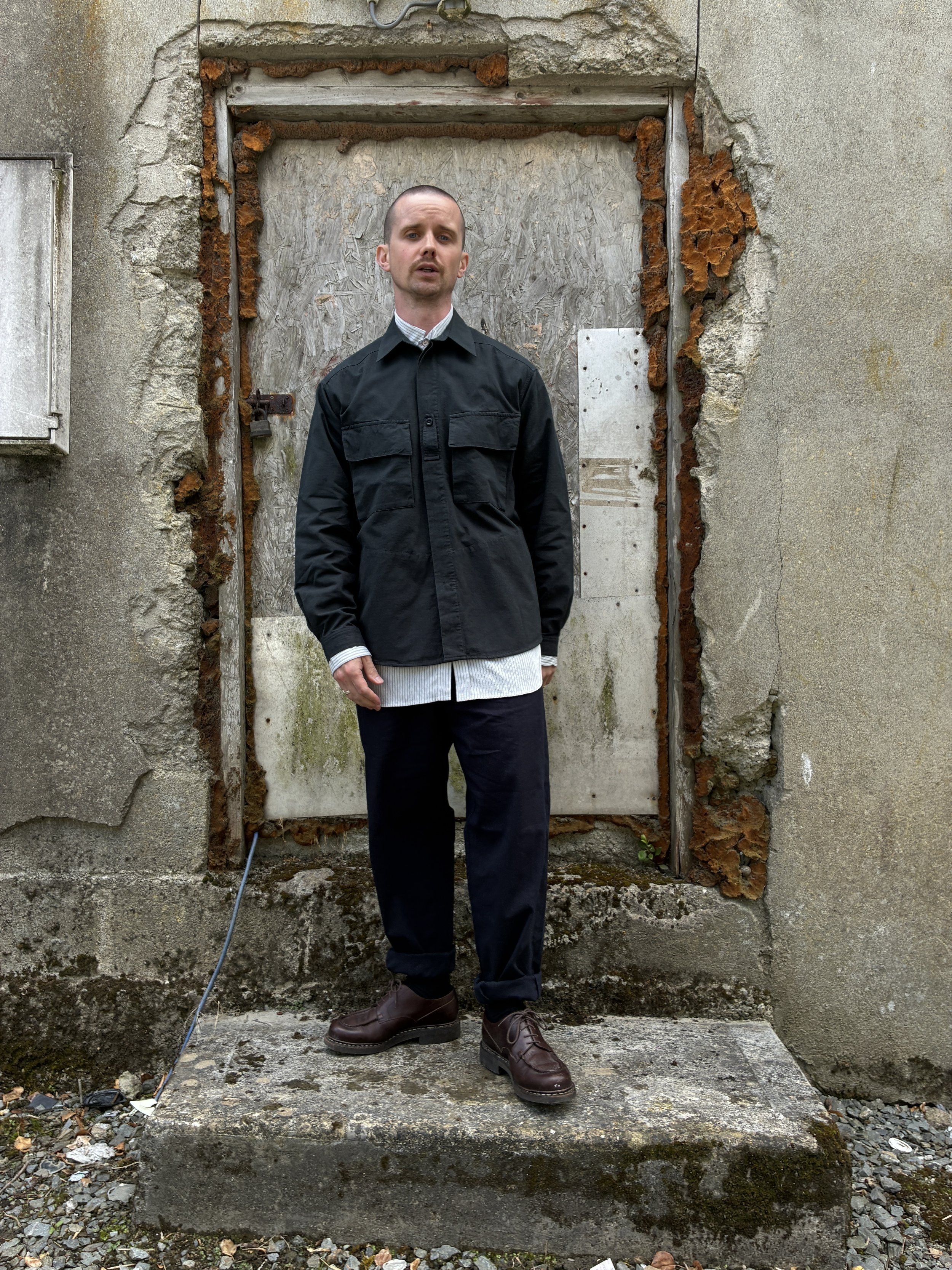 Man in front of wall wearing 1st PAT-RN Sumatra Charcoal Overshirt