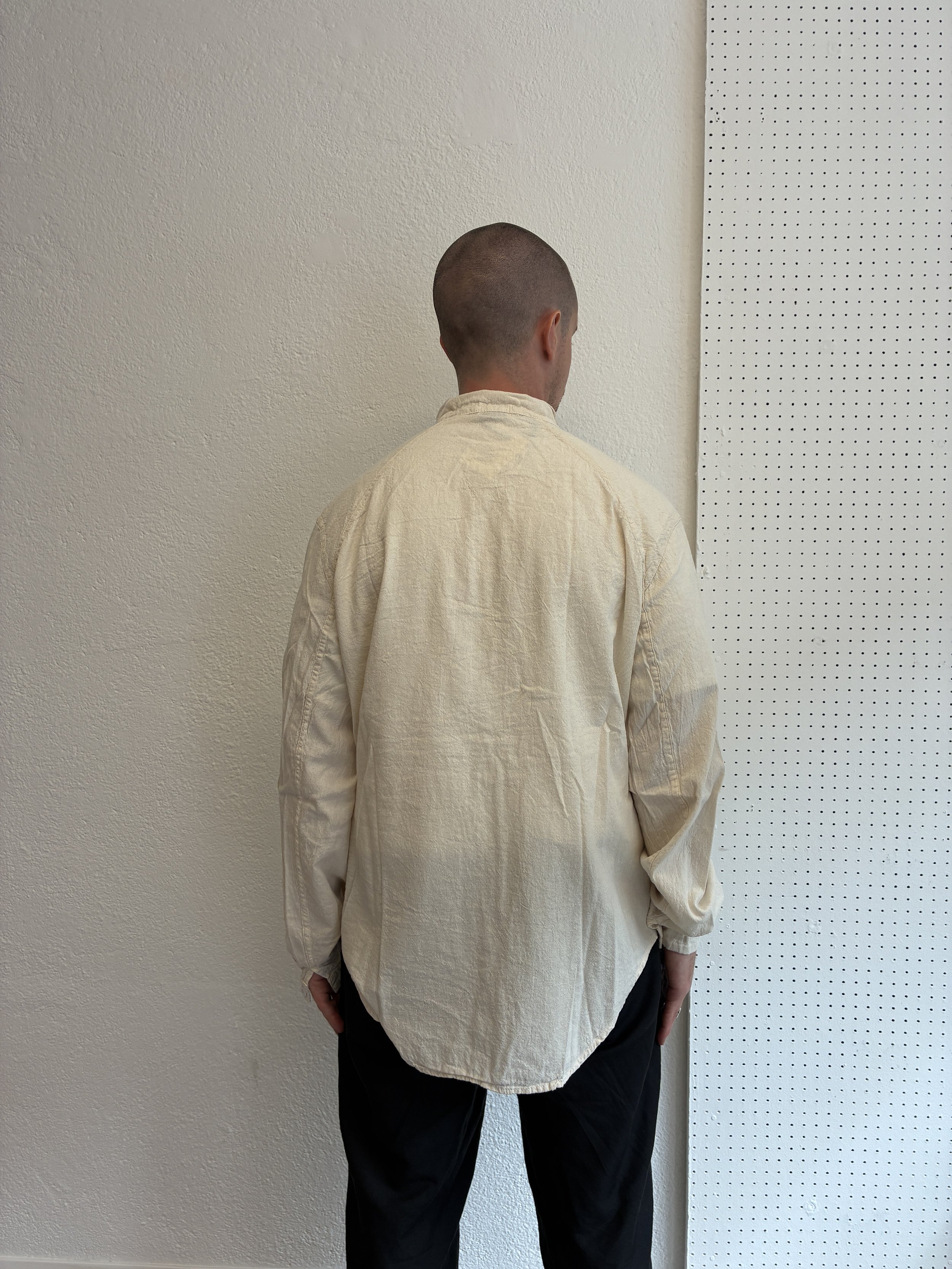 Back of man wearing Tender Co Type 457 ecru rinsed Frock Shirt in front of white wall