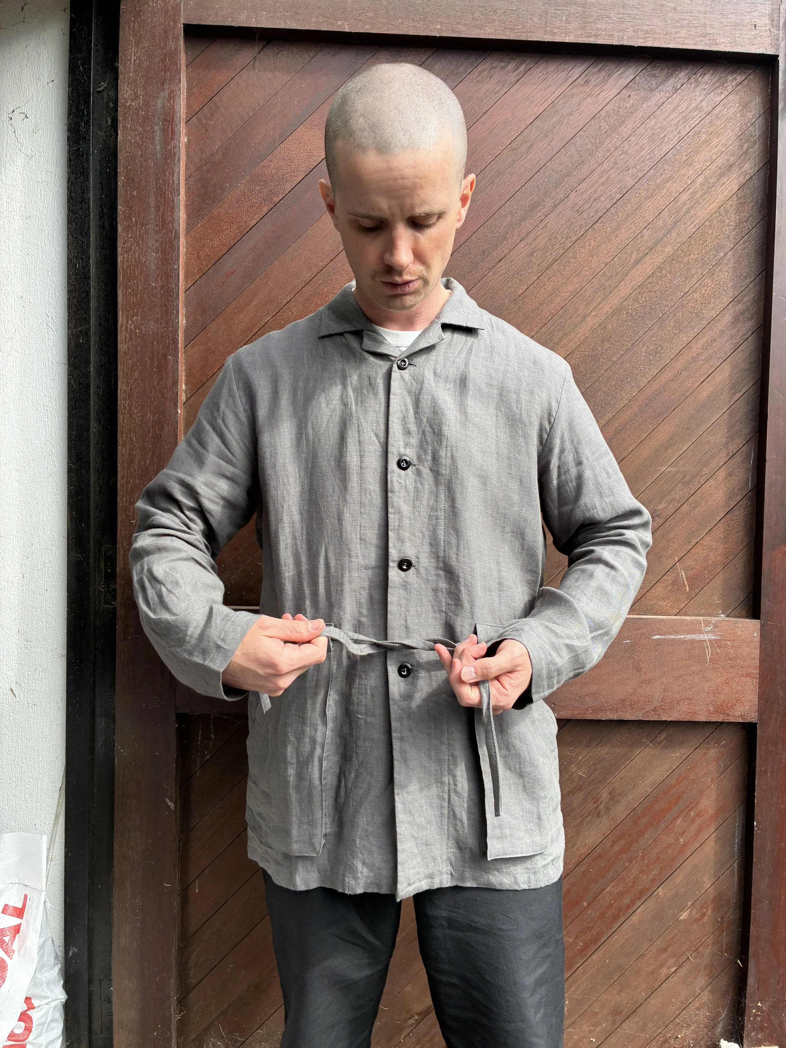 Man in front of wooden door tying the waist of Limited Edition Frank Leder Grey LINDWURM Linen Cardigan