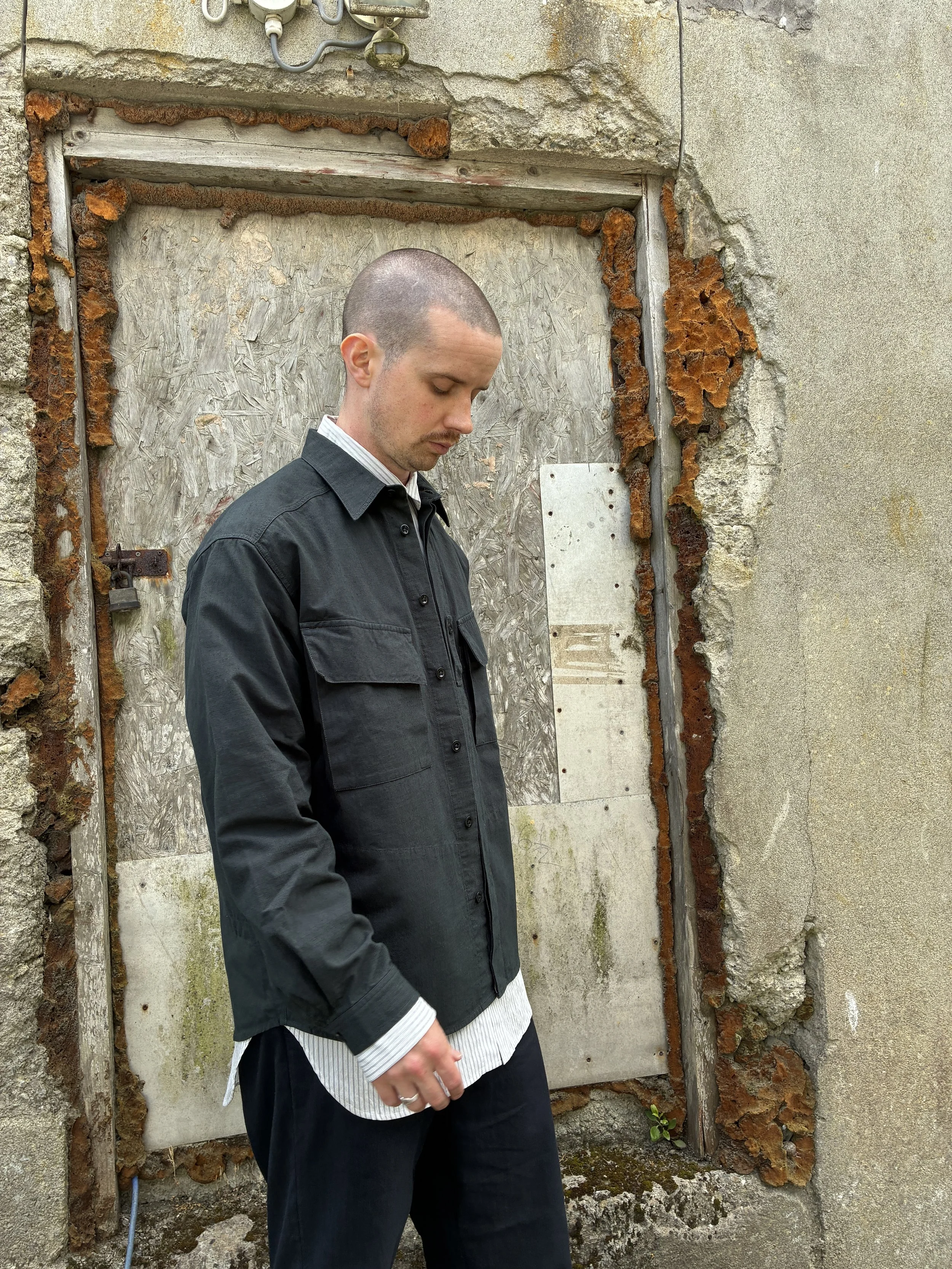 Man in front of wall wearing 1st PAT-RN Sumatra Charcoal Overshirt