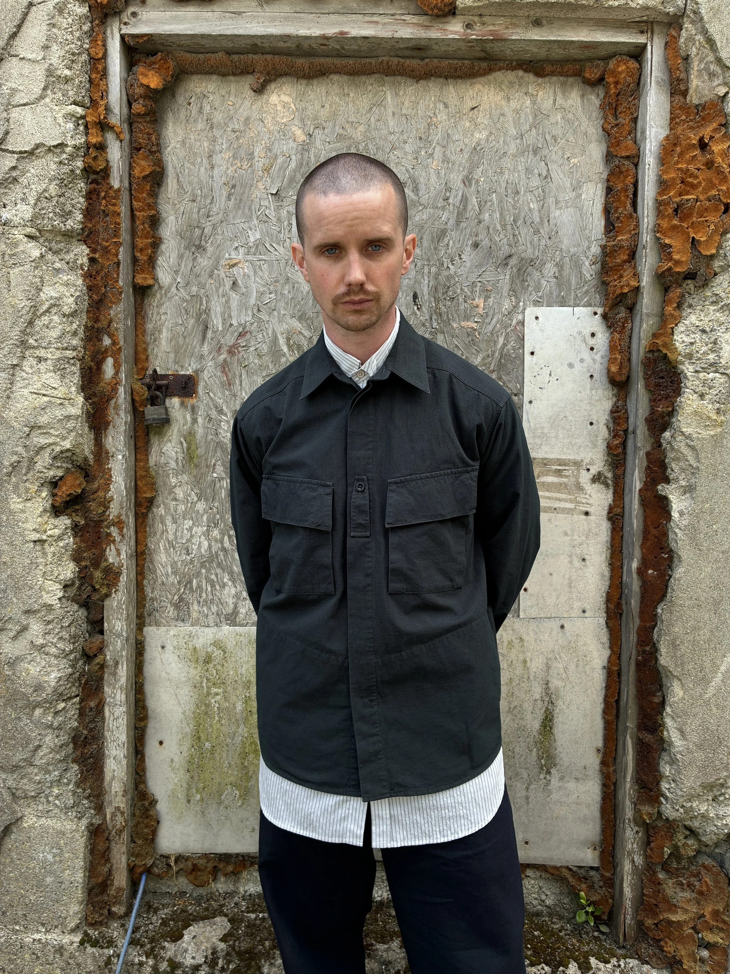 Man in front of wall wearing 1st PAT-RN Sumatra Charcoal Overshirt