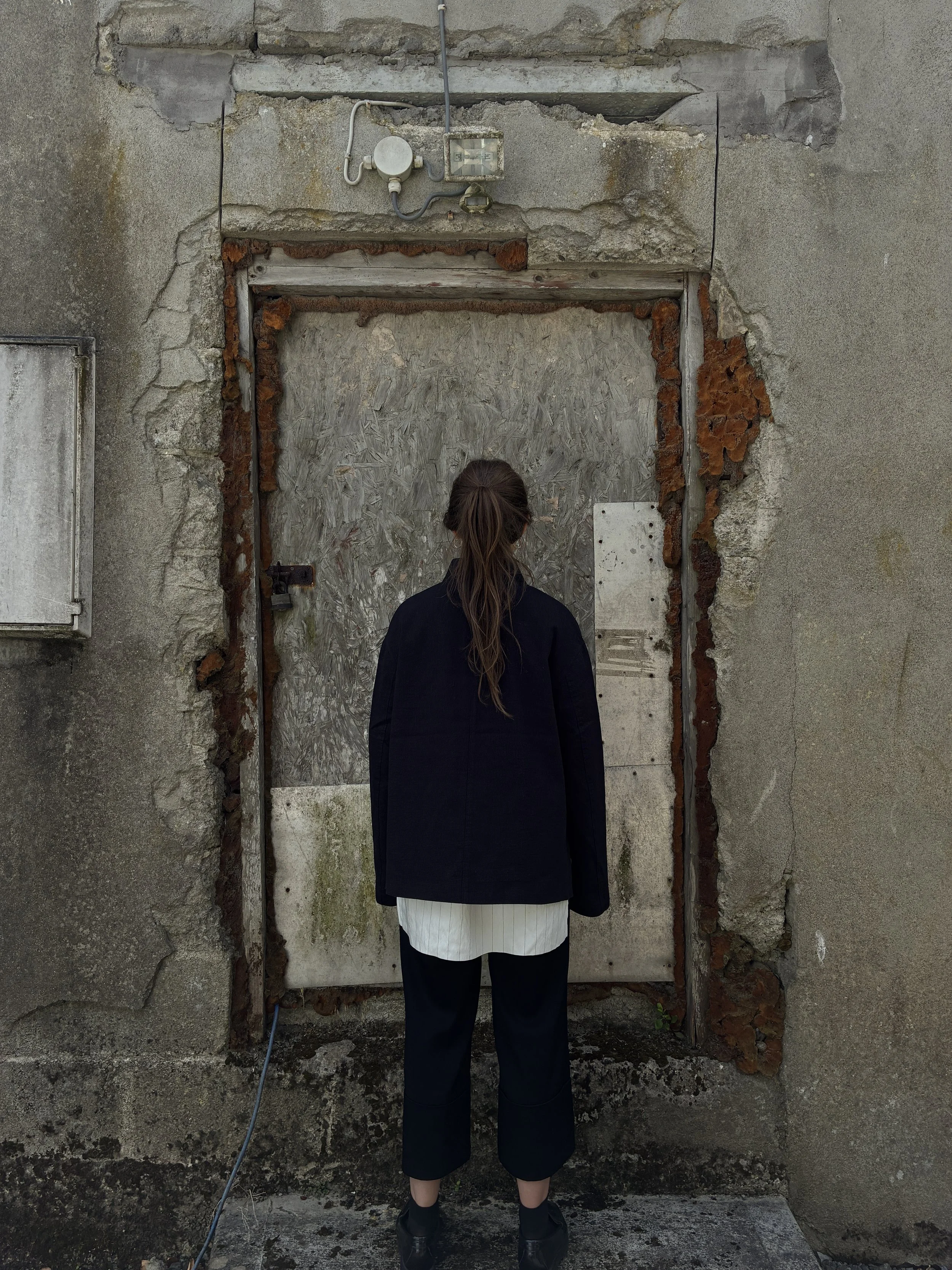 Back of Woman in front of wall wearing Charcoal 1st PAT-RN Woman Rei Jacket