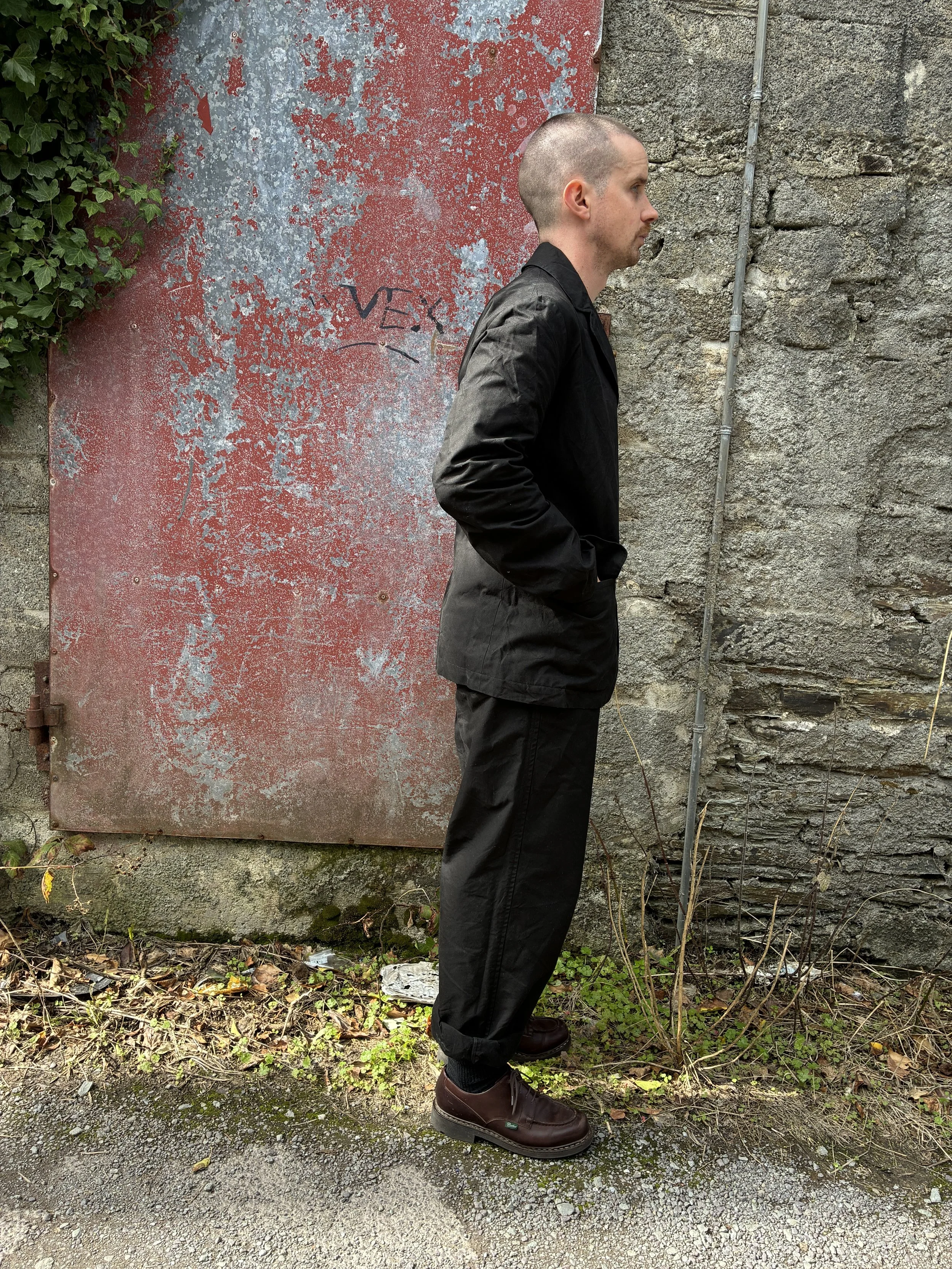 Side of Man in front of red wall outside wearing Black Conkers Rambler Blazer and trousers