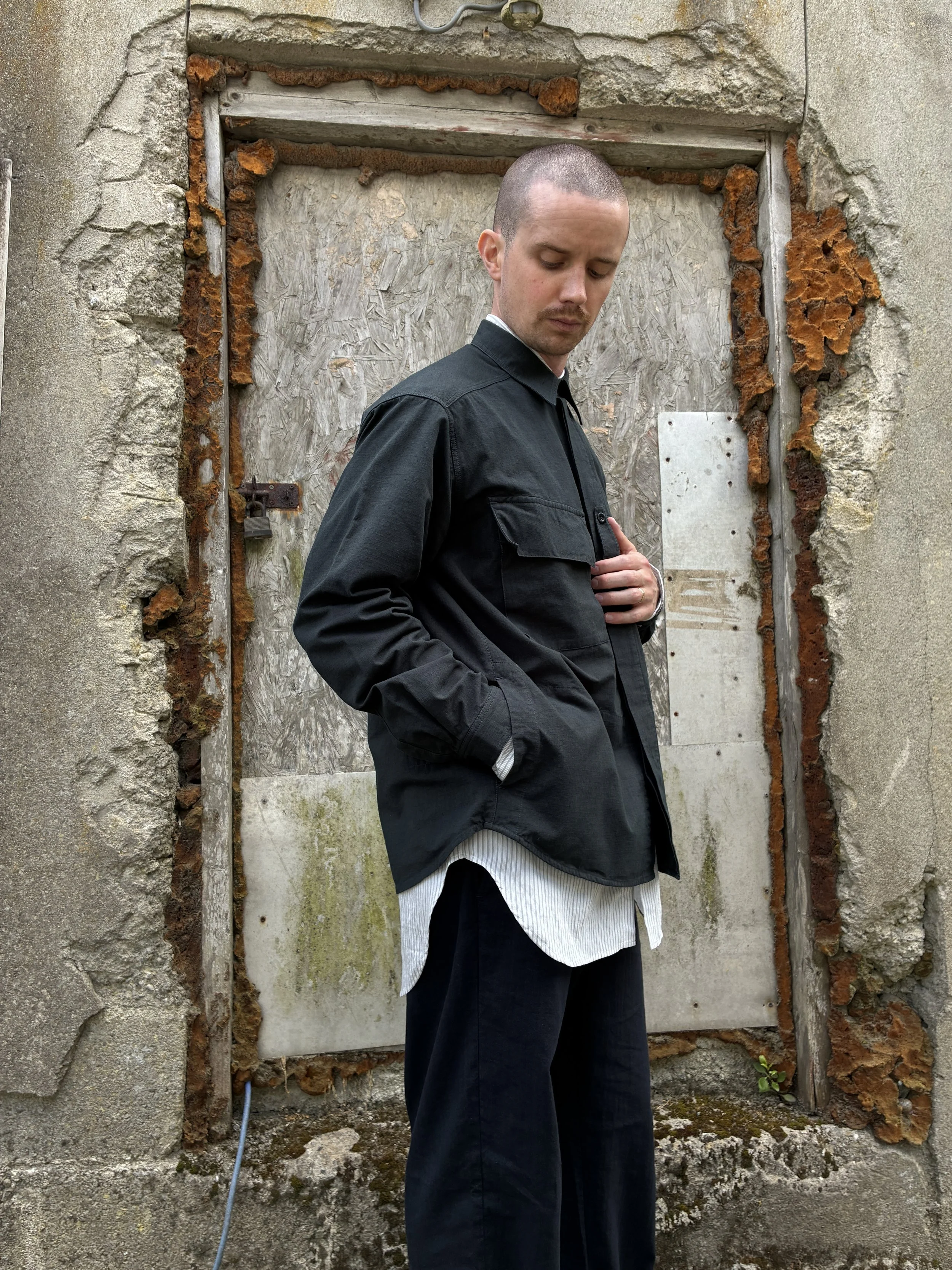 Side of Man in front of wall wearing 1st PAT-RN Sumatra Charcoal Overshirt
