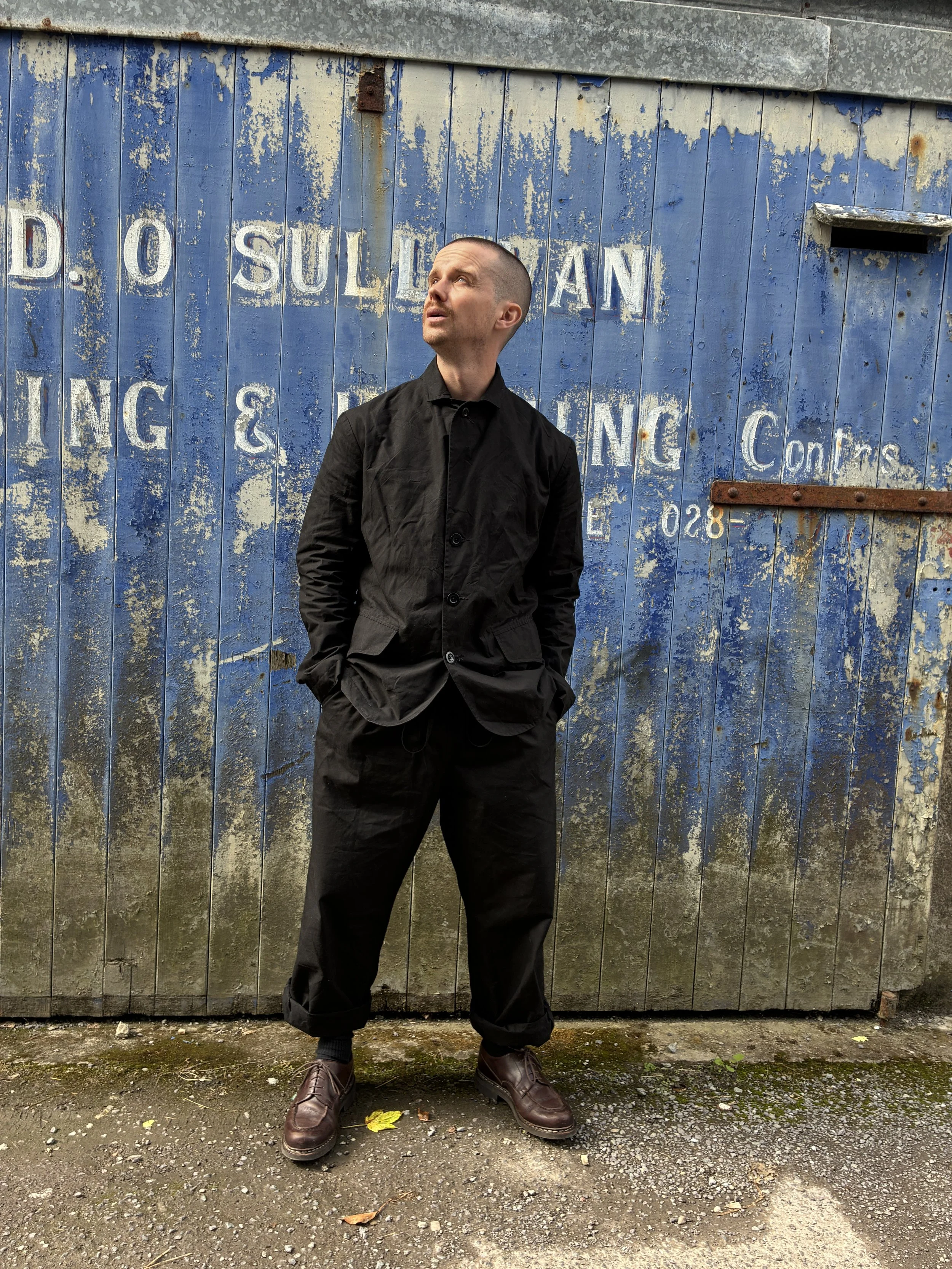 Man in front of blue rusty door outside wearing Black Conkers Rambler Blazer and trousers