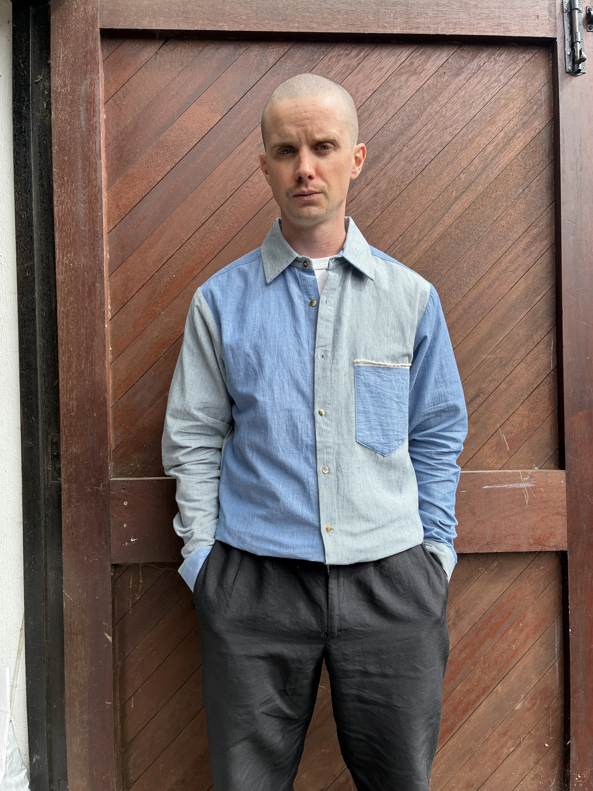 Man in front of door wearing Frank Leder Blue Patchwork Vintage Fabric Edition Shirt tucked into black trousers
