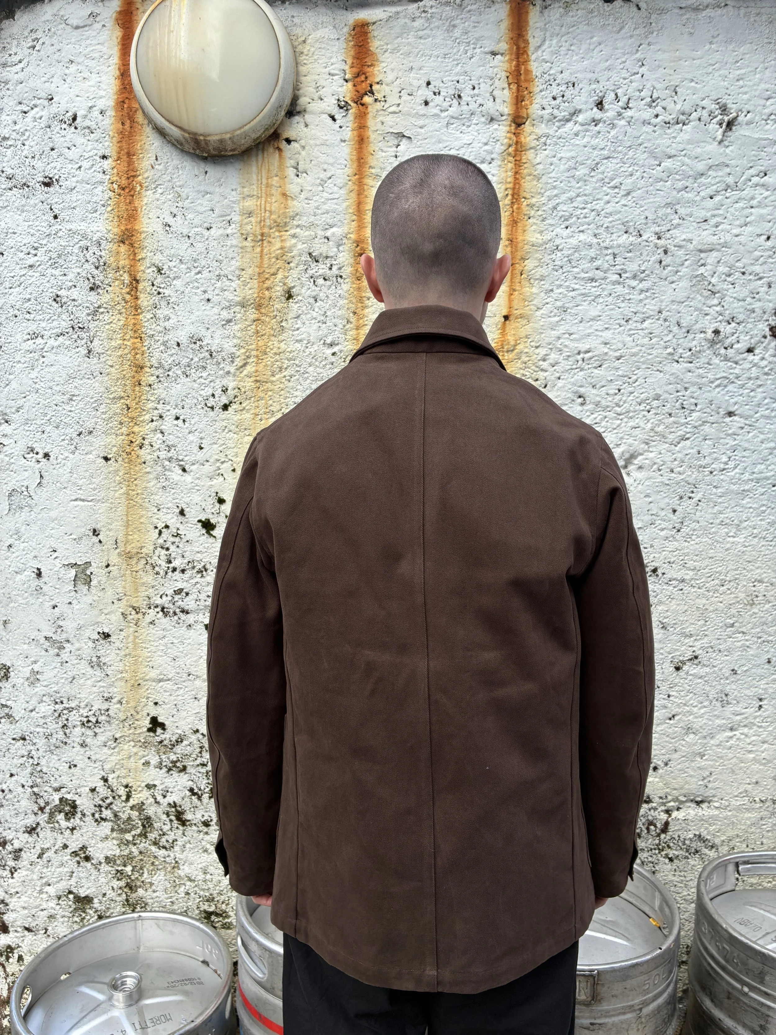 Back of man in front of rusty wall wearing brown Conkers Bruton Blazer Jacket