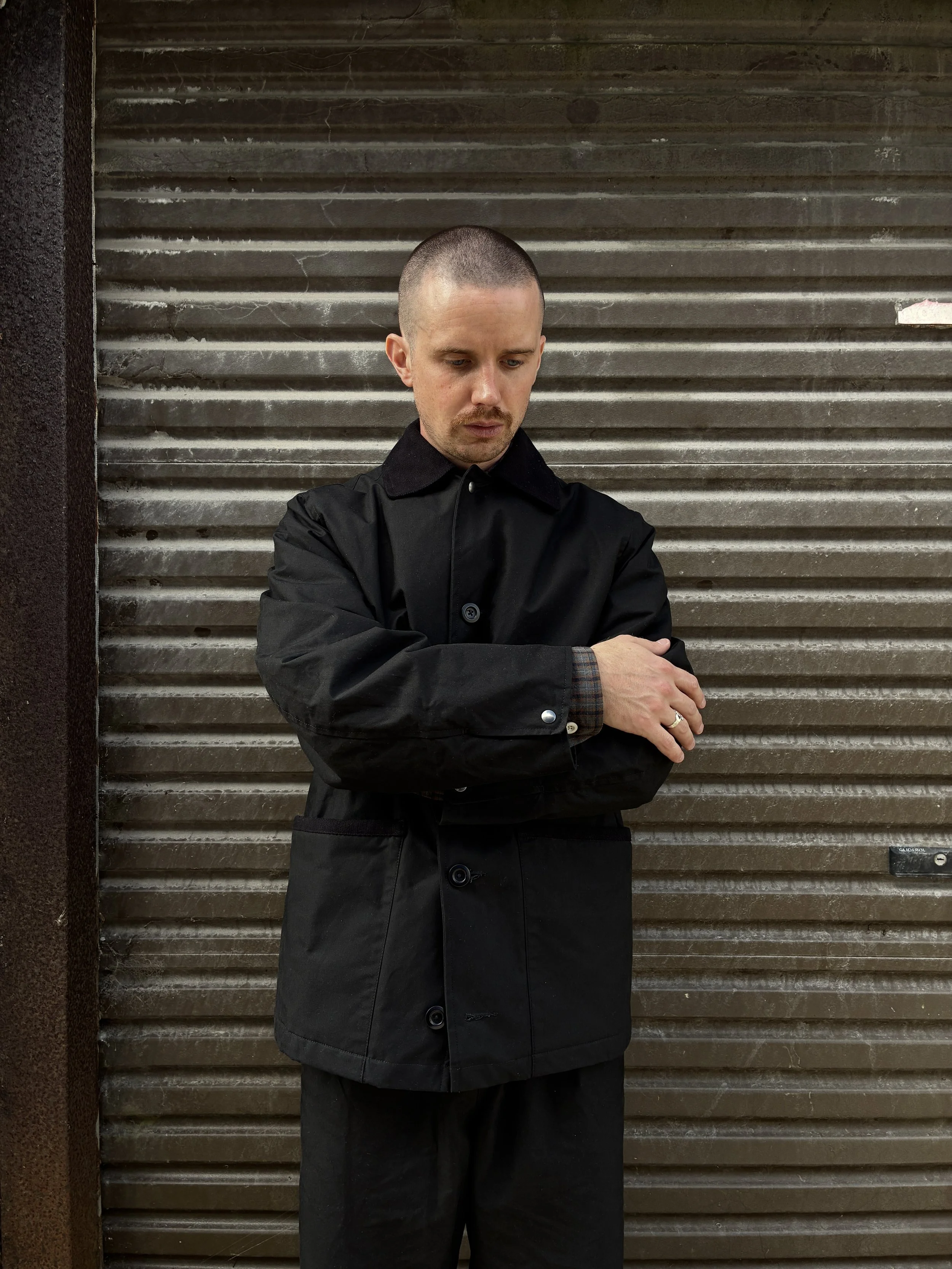 Man wearing Black Conkers Blanket Jacket in front of shutters with arms folded