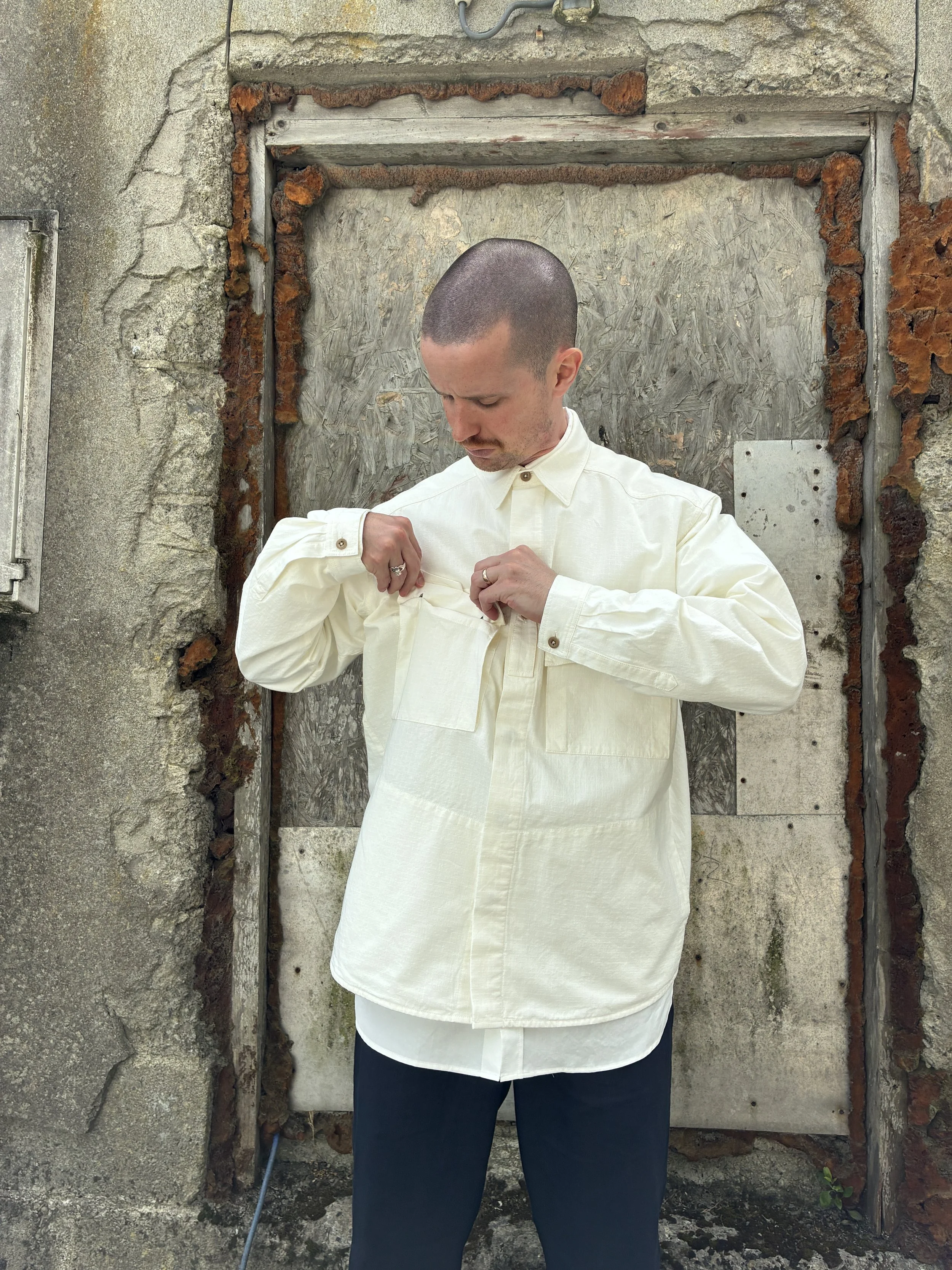 Man in front of wall looking into pocket of Off-White Ecru 1st PAT-RN Sumatra Overshirt