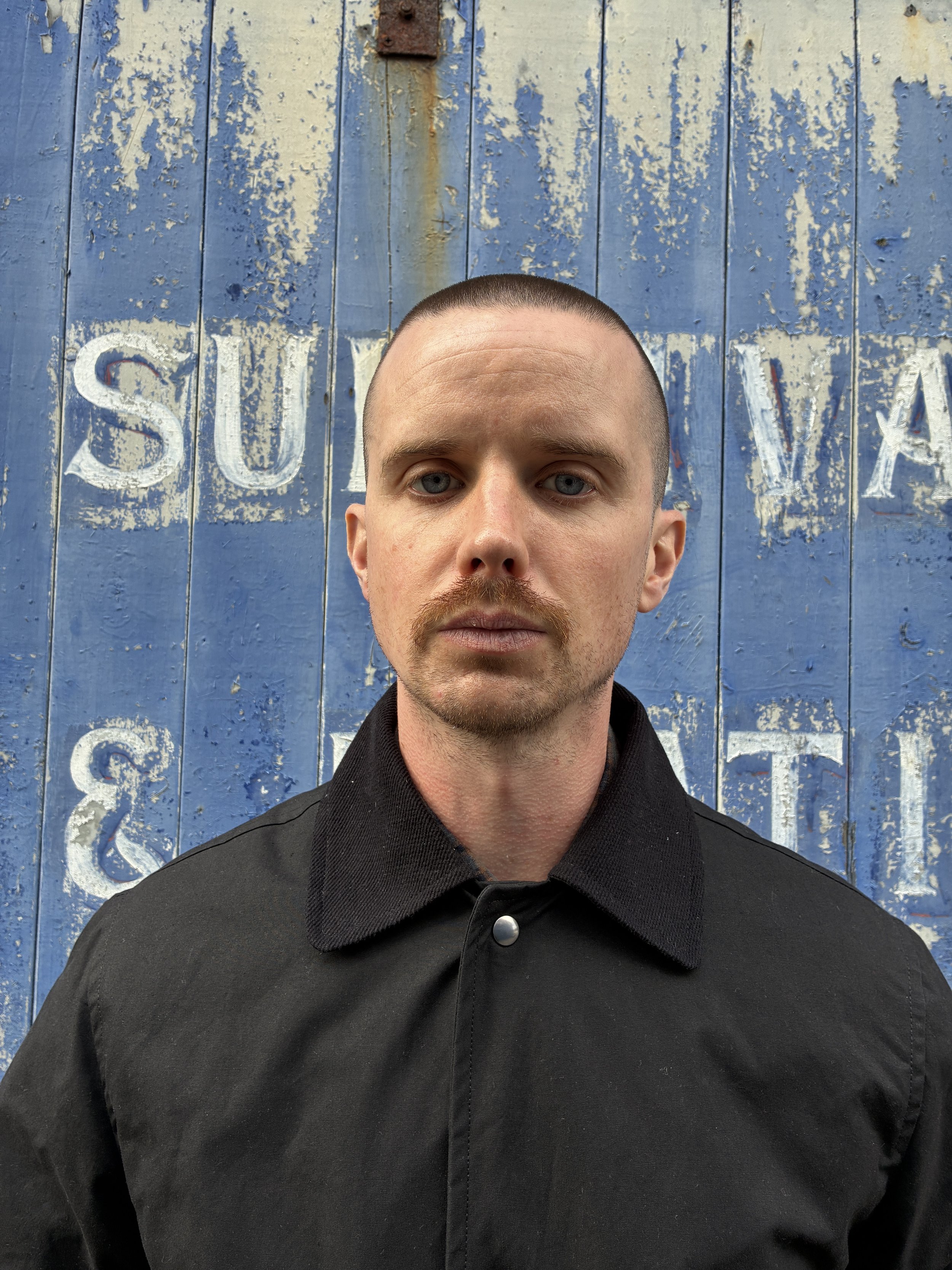 Closeup of Man wearing Black Conkers Blanket Jacket in front of blue graffiti