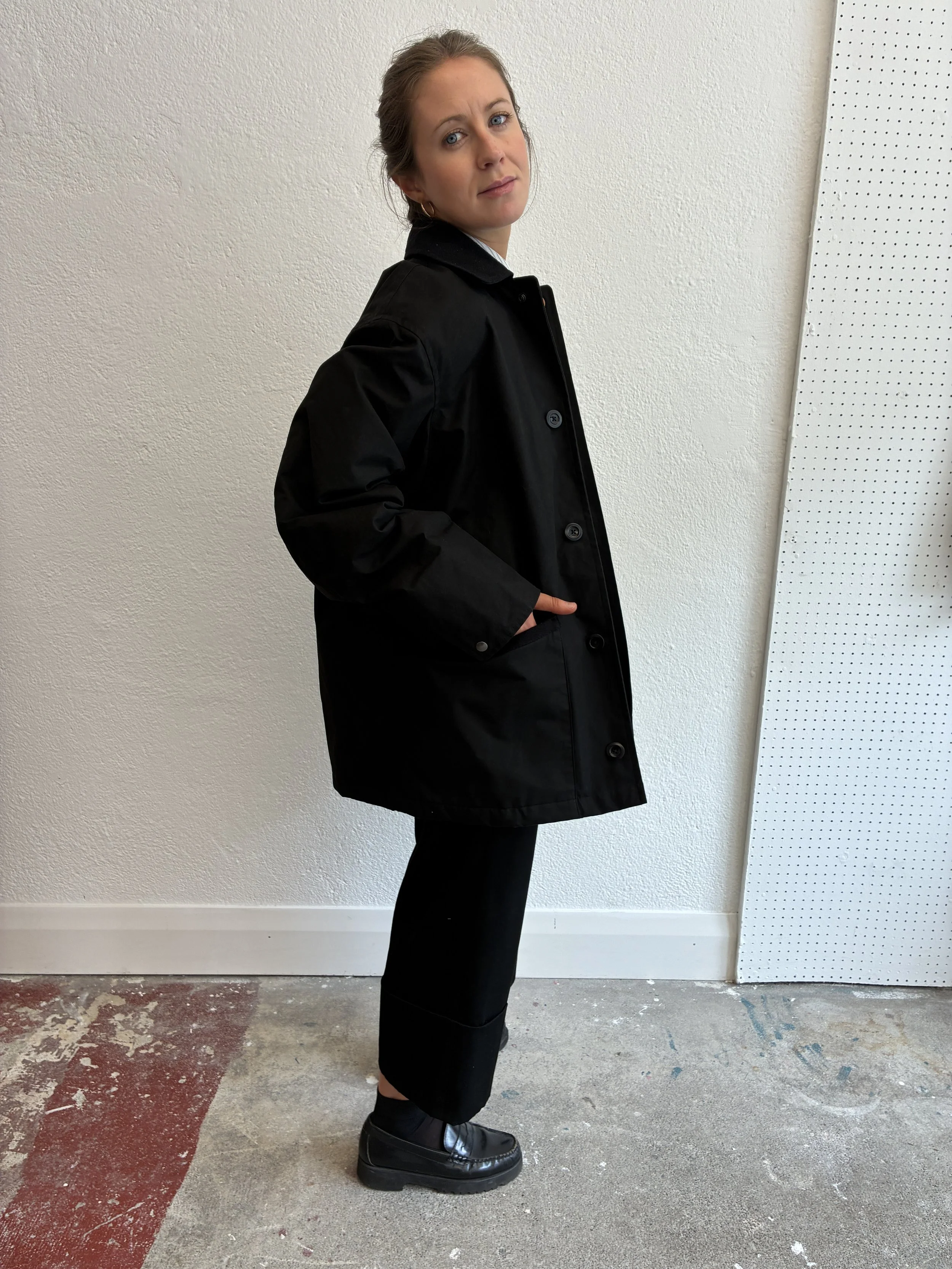 Side of Woman wearing Black Conkers Blanket Jacket in front of white wall