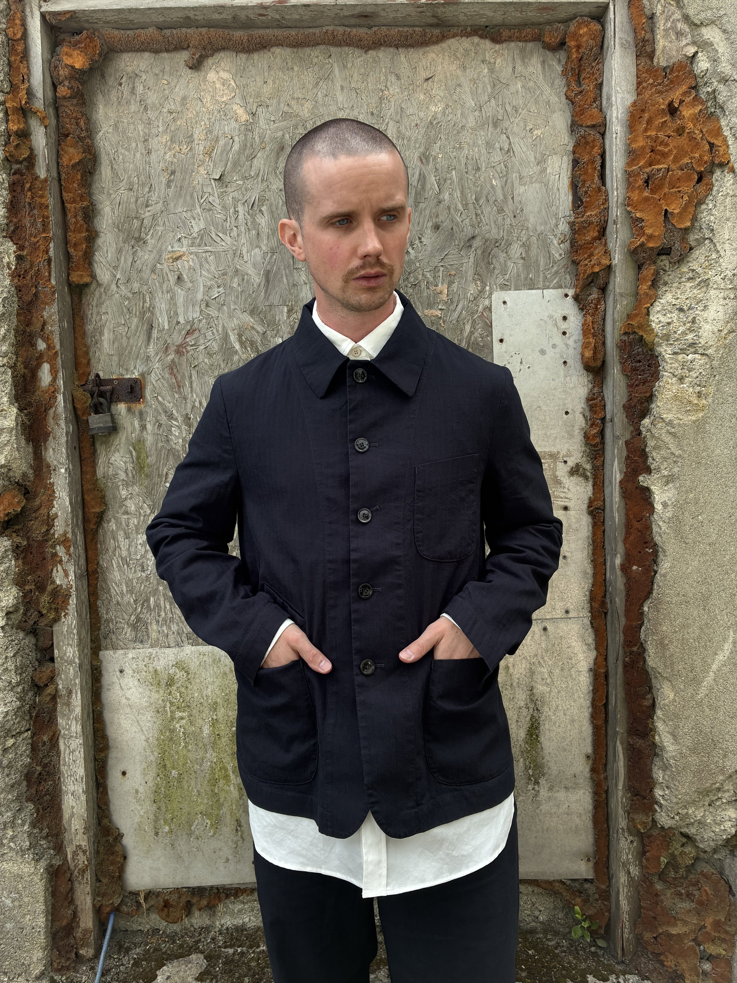 Man in front of wall wearing Navy 1st PAT-RN Notion Jacket with hands in pockets