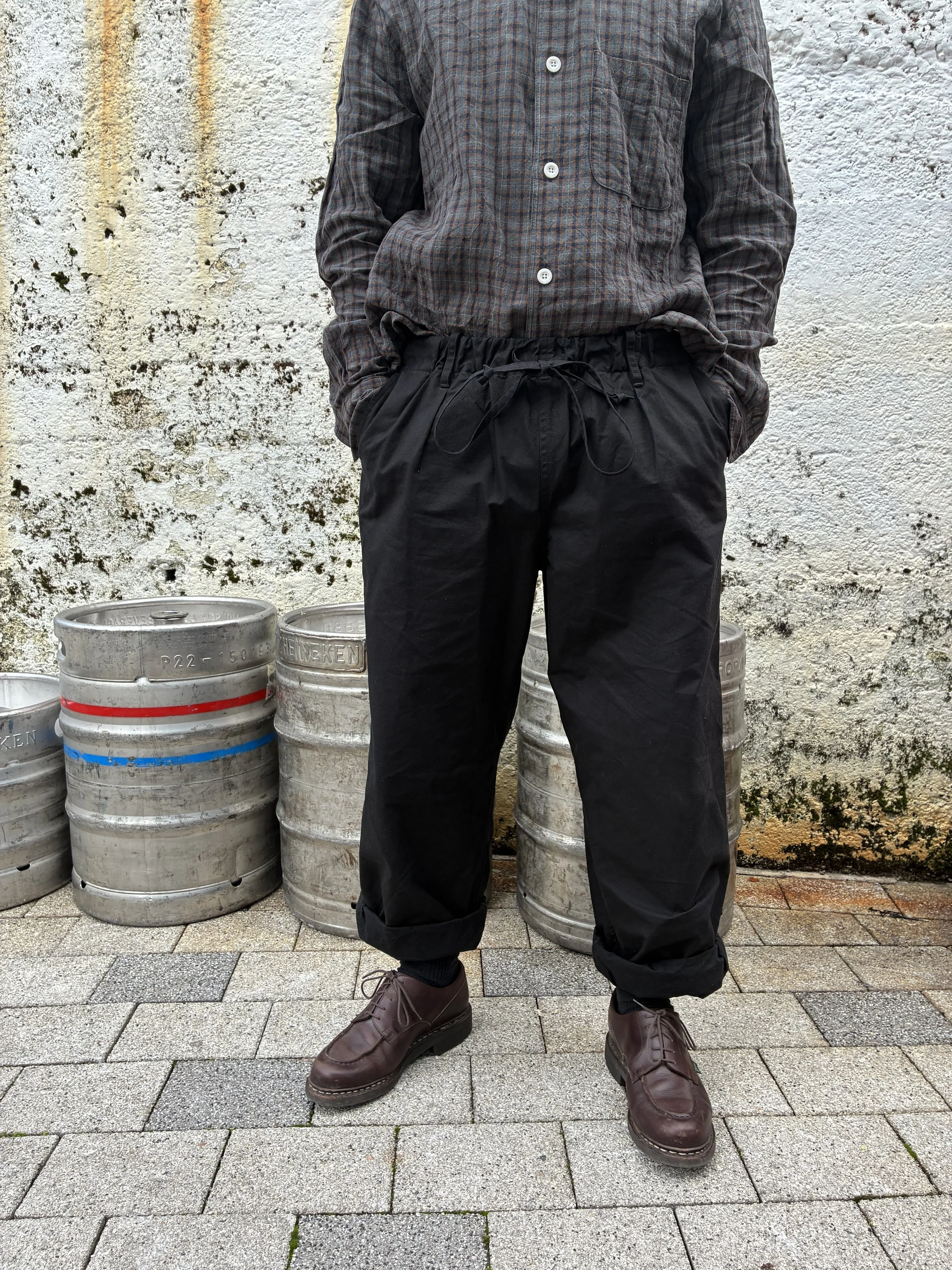 Man wearing Conkers Rambler Black Waxed Cotton Trousers in front of beer kegs