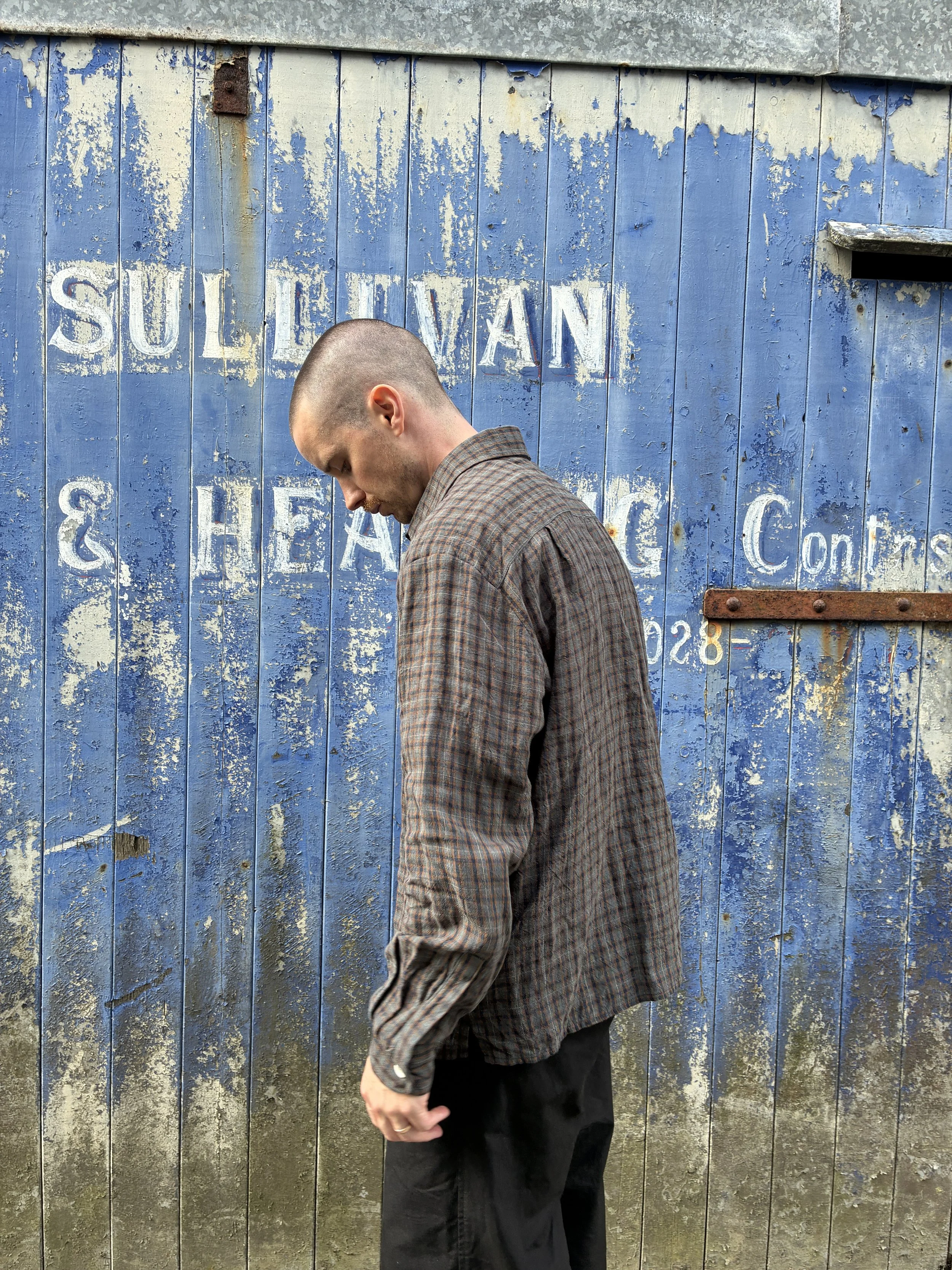 Side of man wearing Dusk Conkers Relaxed Farmer Shirt in front of rusty blue shutter