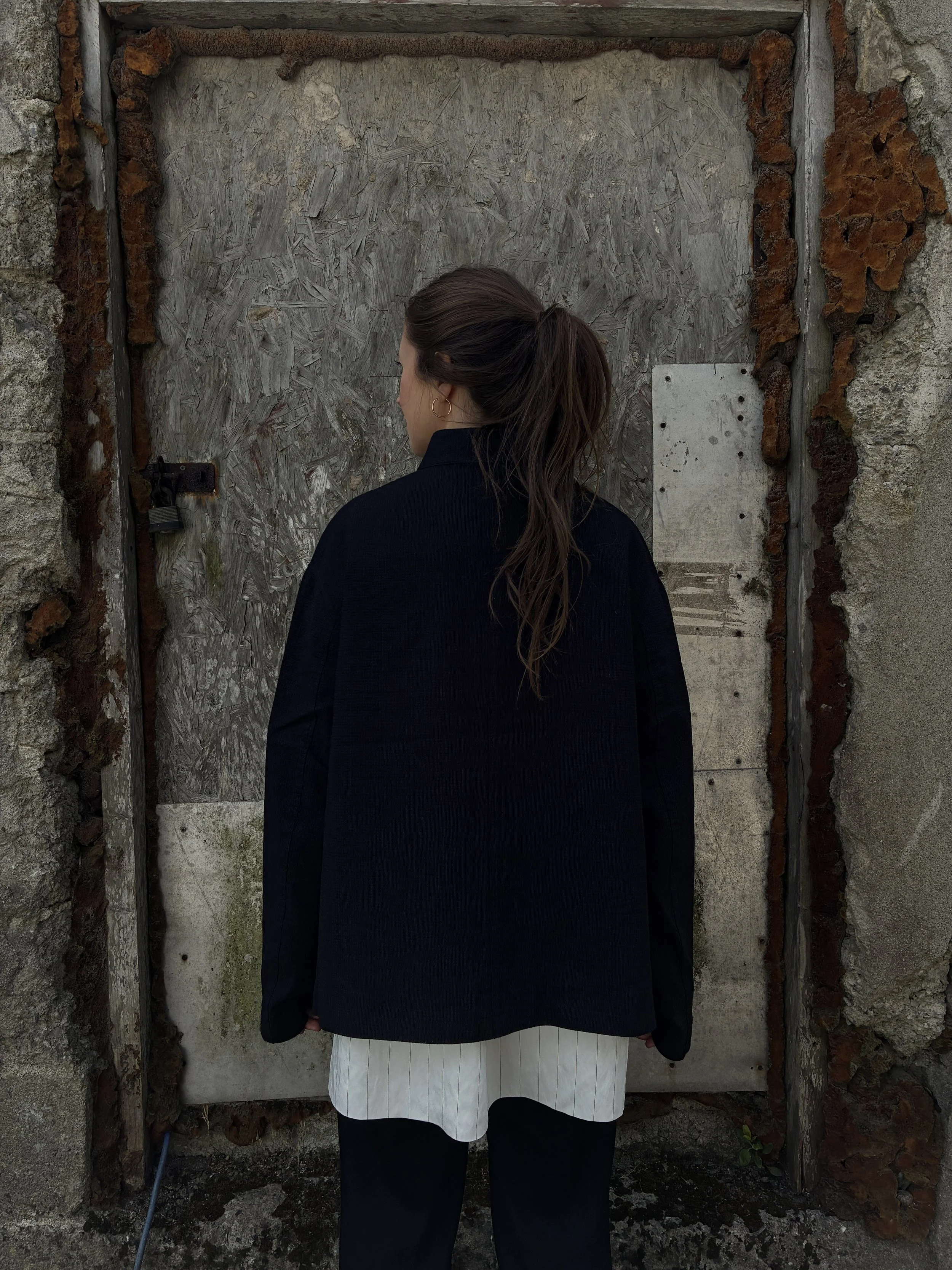 Back of Woman in front of wall wearing Charcoal 1st PAT-RN Woman Rei Jacket