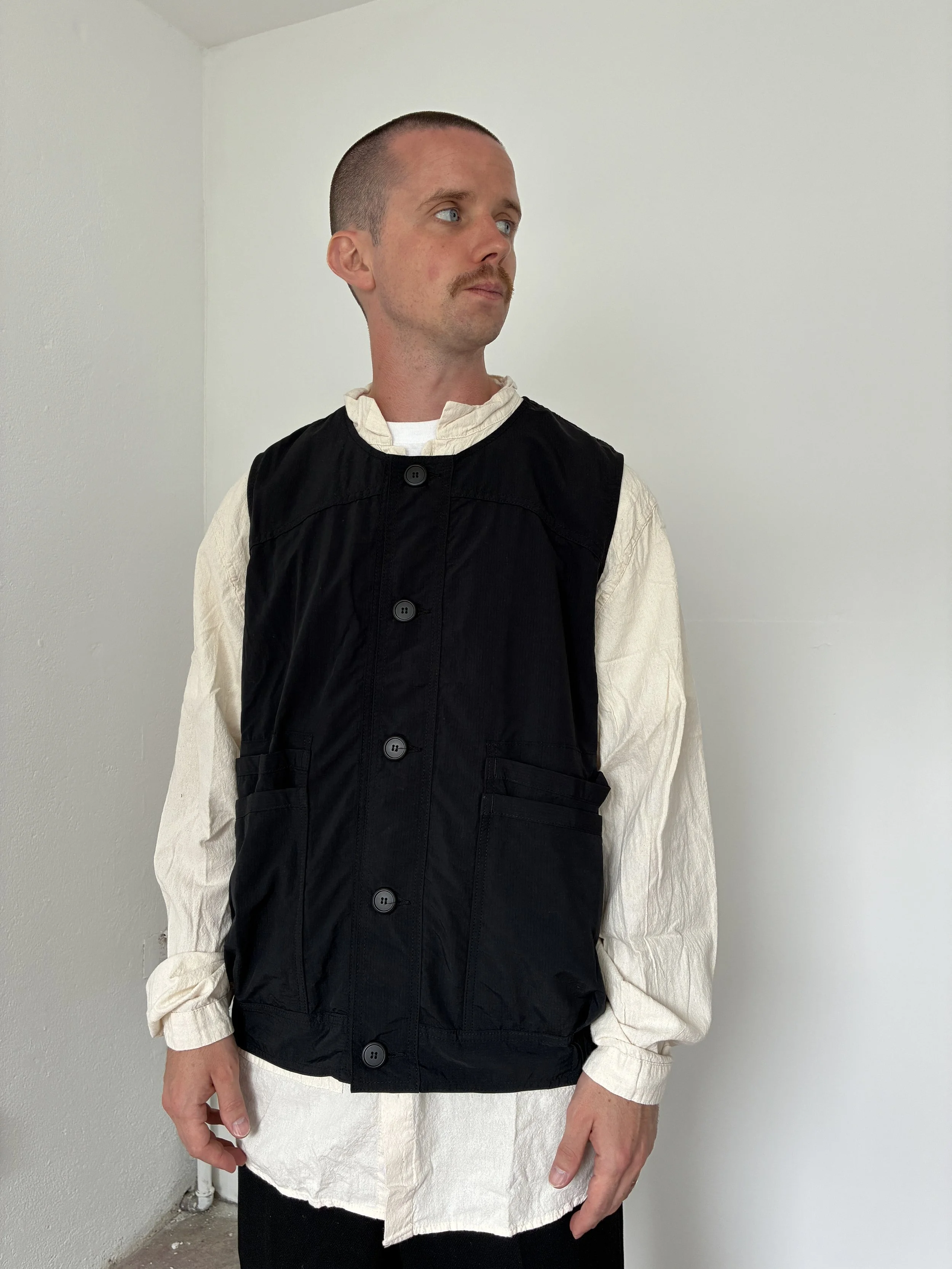 Man wearing Black Sassafras Overgrown Hiker Vest in front of concrete wall