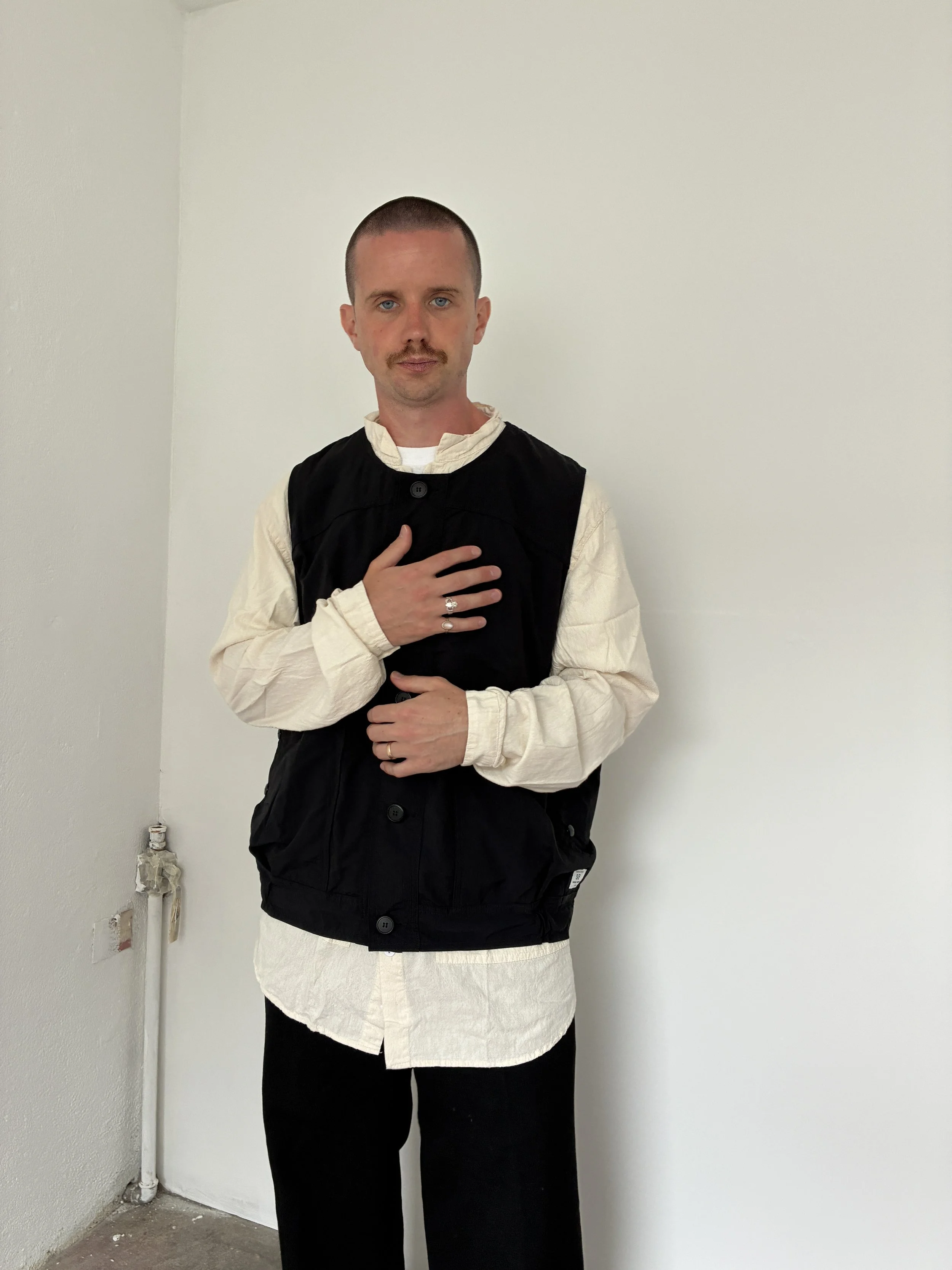 Man wearing Black Sassafras Overgrown Hiker Vest in front of concrete wall