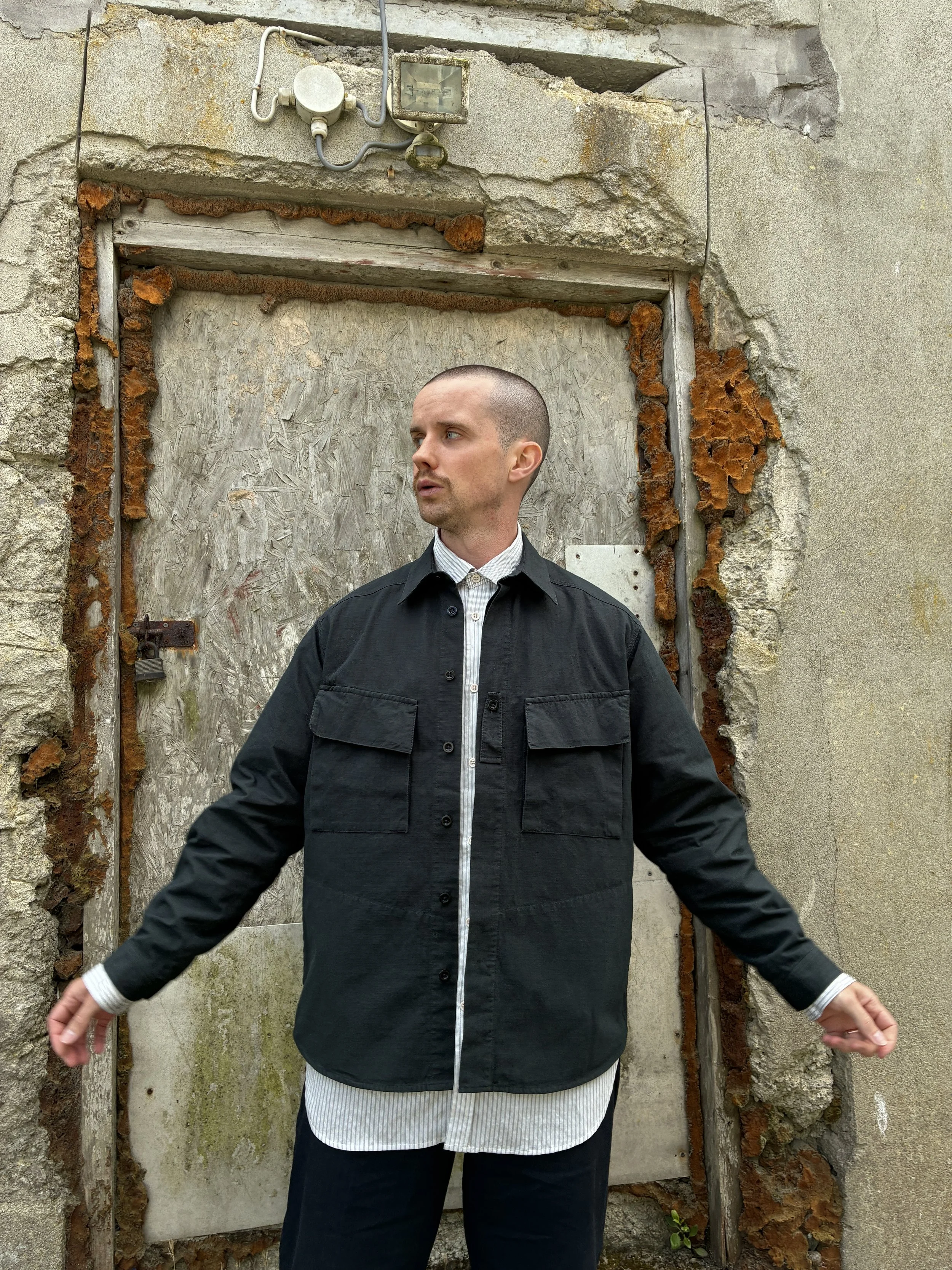 Man in front of wall wearing 1st PAT-RN Sumatra Charcoal Overshirt