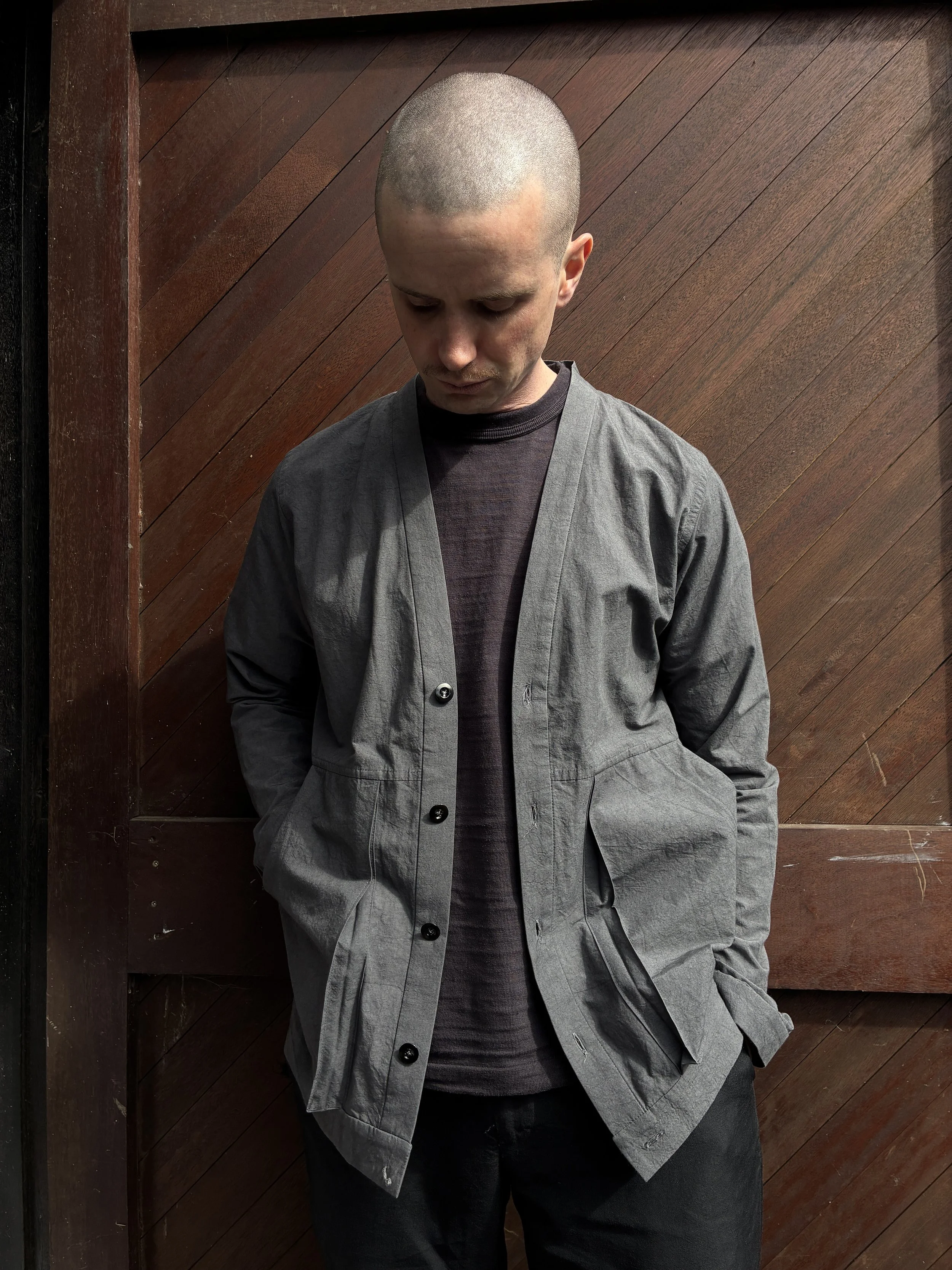 Man in front of wooden door wearing Frank Leder Grey Japanese Cotton Cardigan looking to the ground