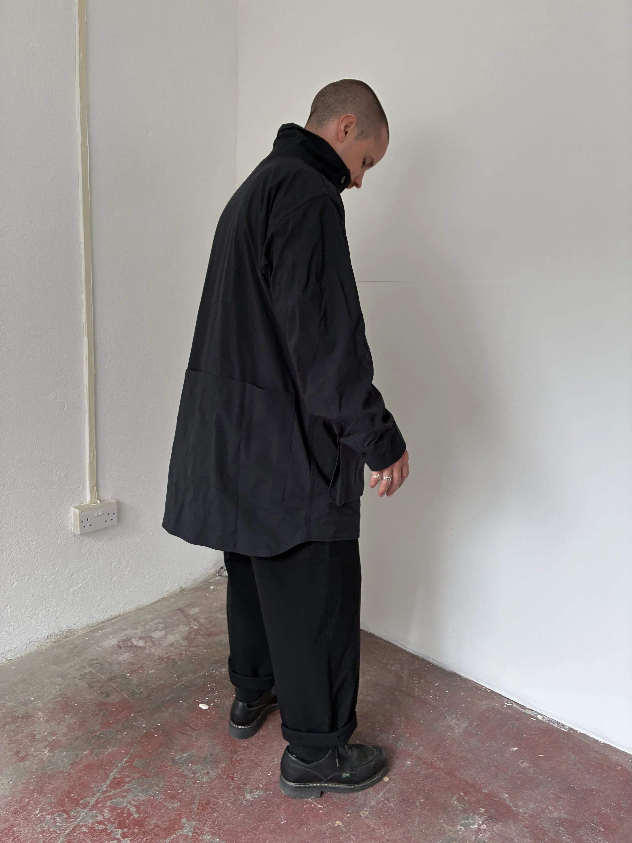 Side profile of Man wearing Black Sassafras Cultivator Coat standing on concrete floor