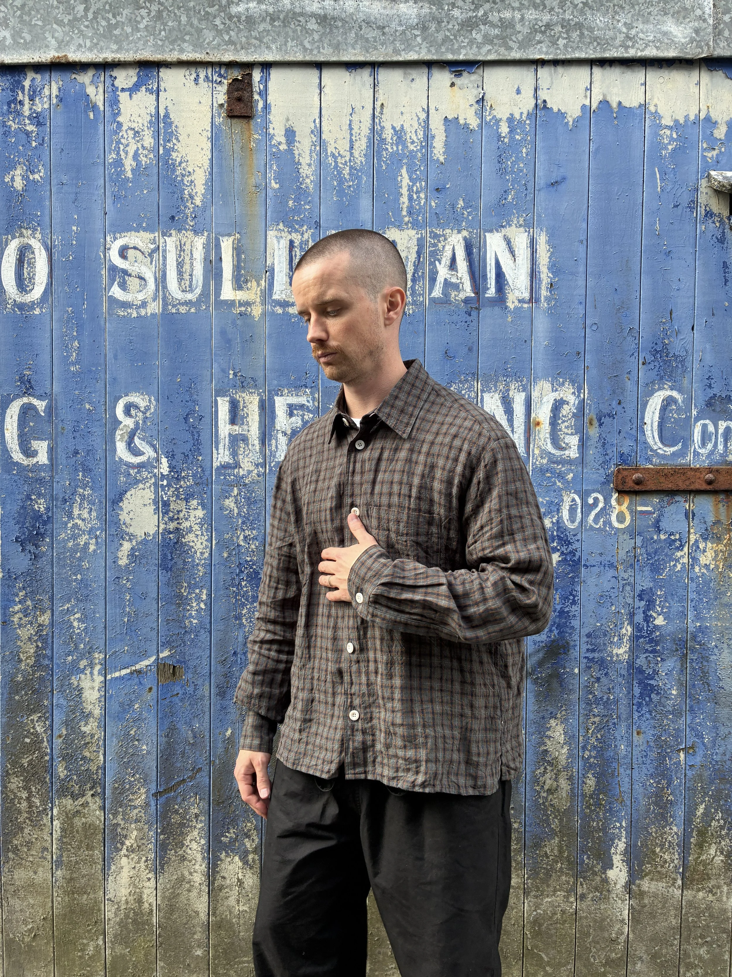Man wearing Dusk Conkers Relaxed Farmer Shirt in front of rusty blue shutter