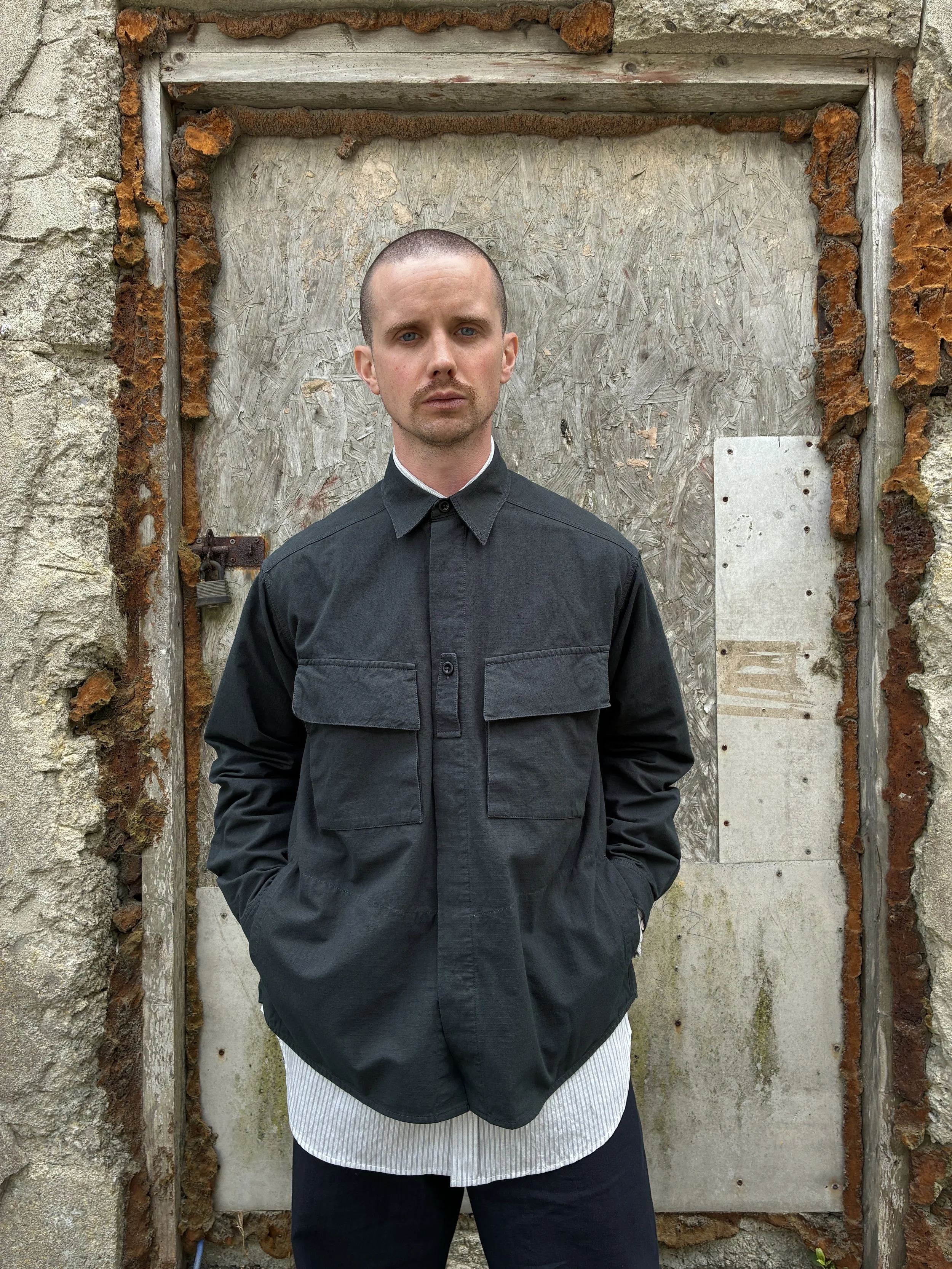 Man in front of wall wearing 1st PAT-RN Sumatra Charcoal Overshirt