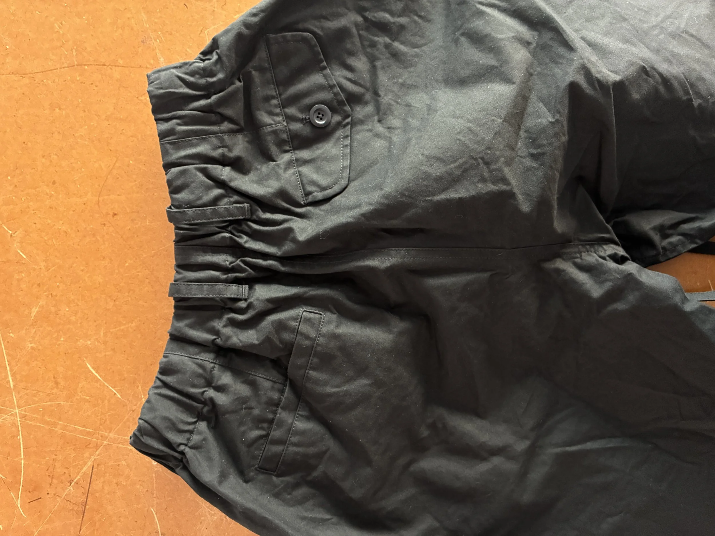 Back of Conkers Rambler Black Waxed Cotton Trousers folded on brown table