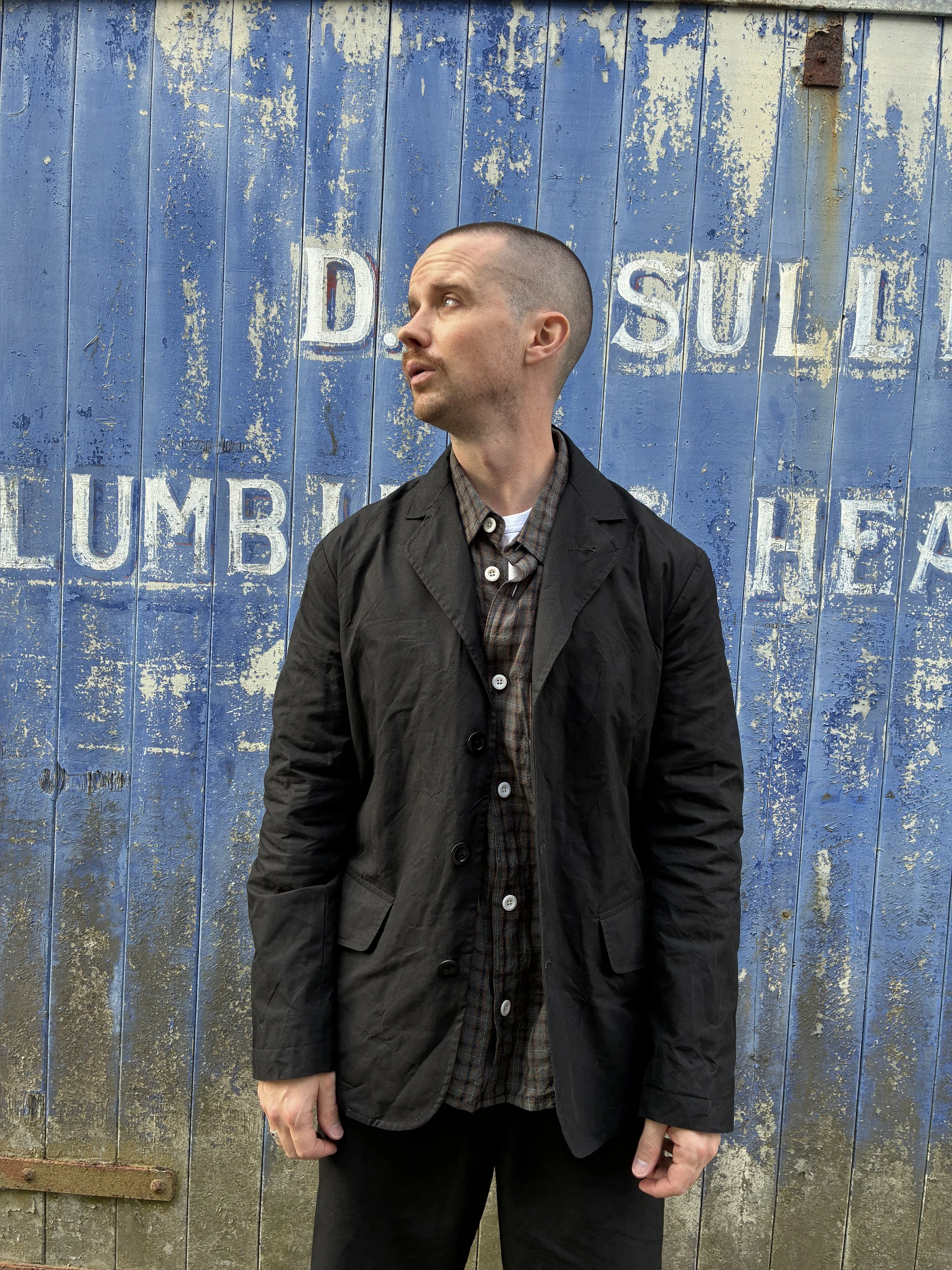 Man in front of blue rusty door outside wearing Black Conkers Rambler Blazer and trousers