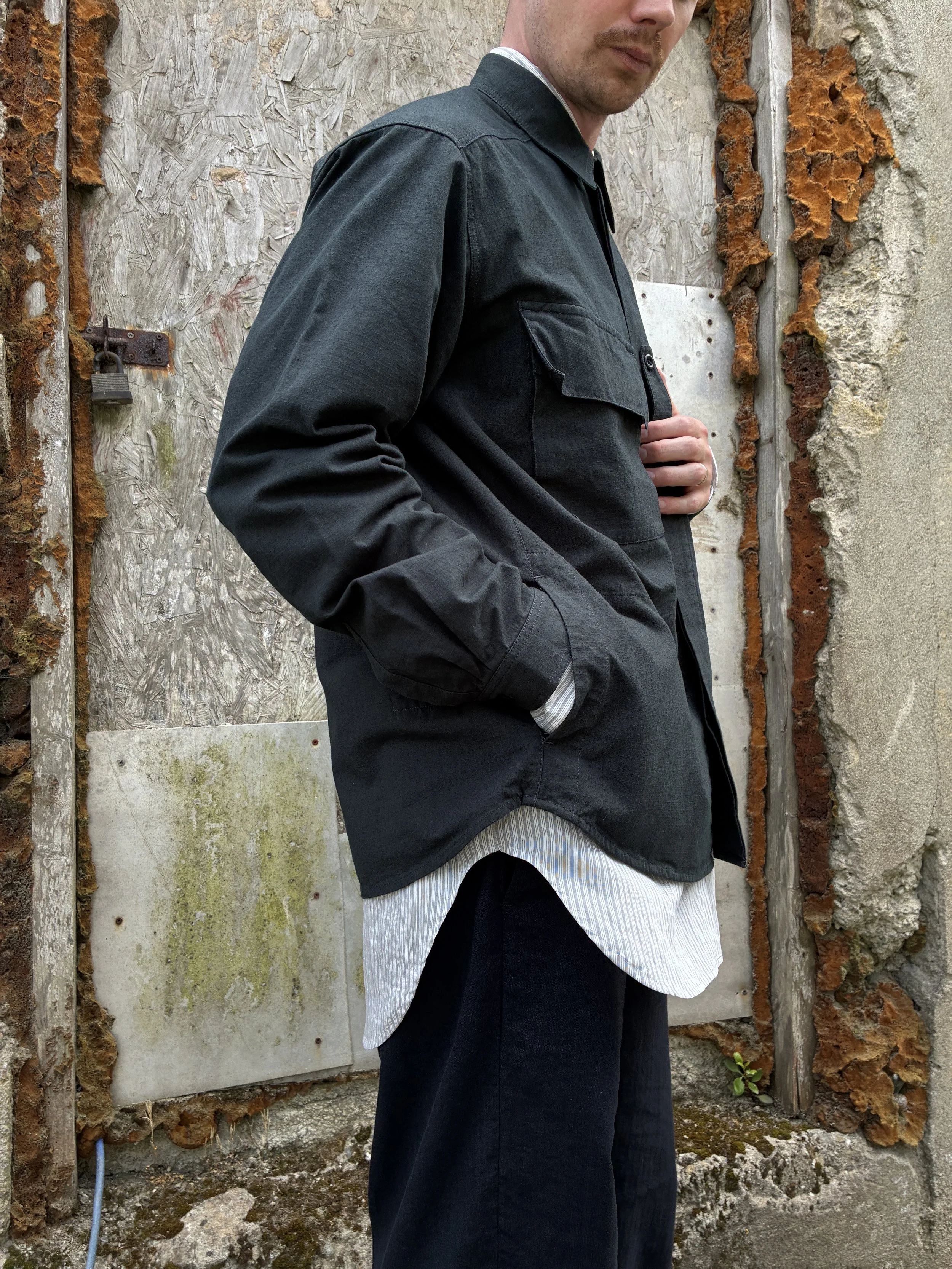 Side of Man in front of wall wearing 1st PAT-RN Sumatra Charcoal Overshirt