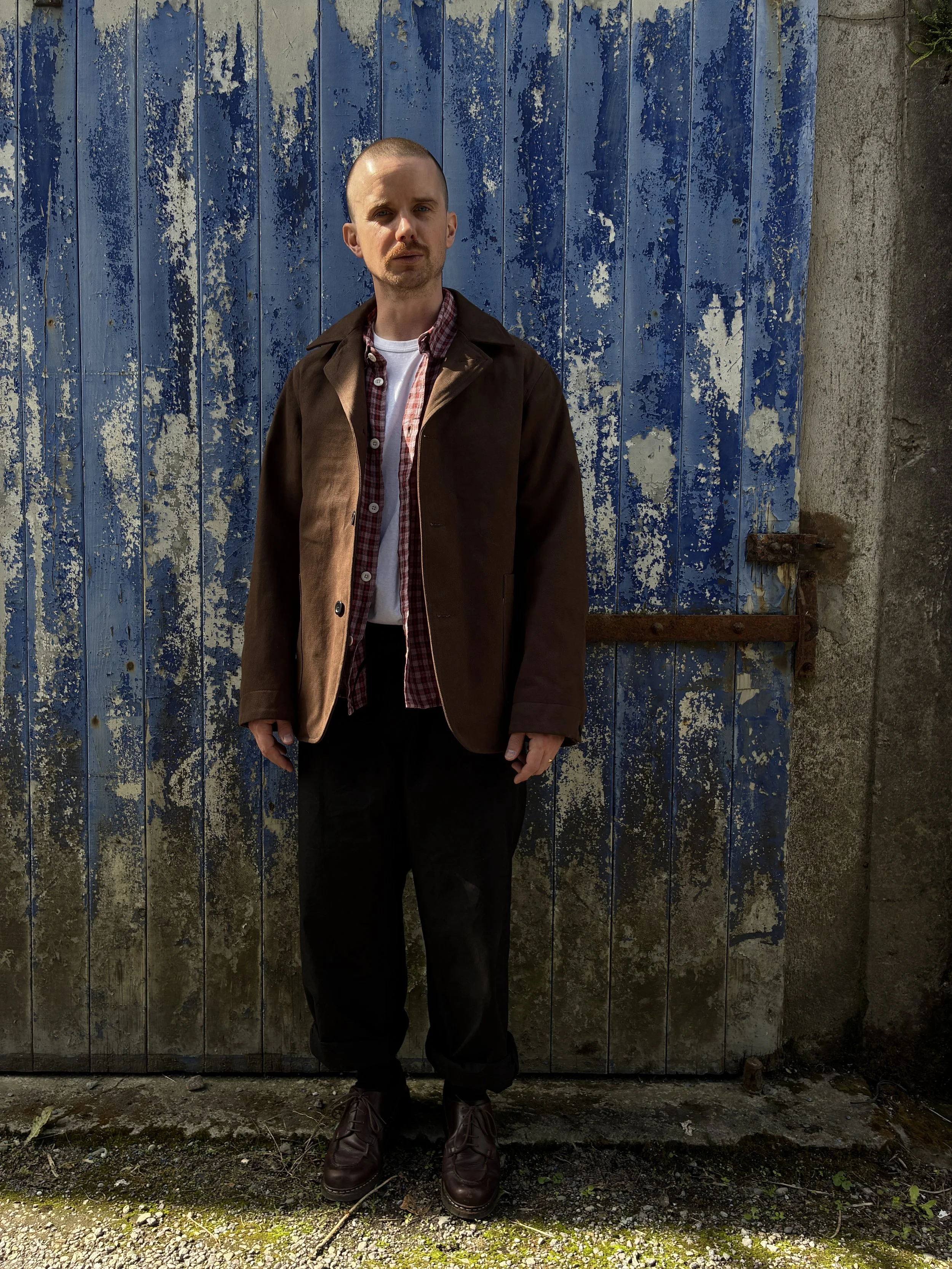 Man in front of blue rusty door wearing brown Conkers Bruton Blazer Jacket