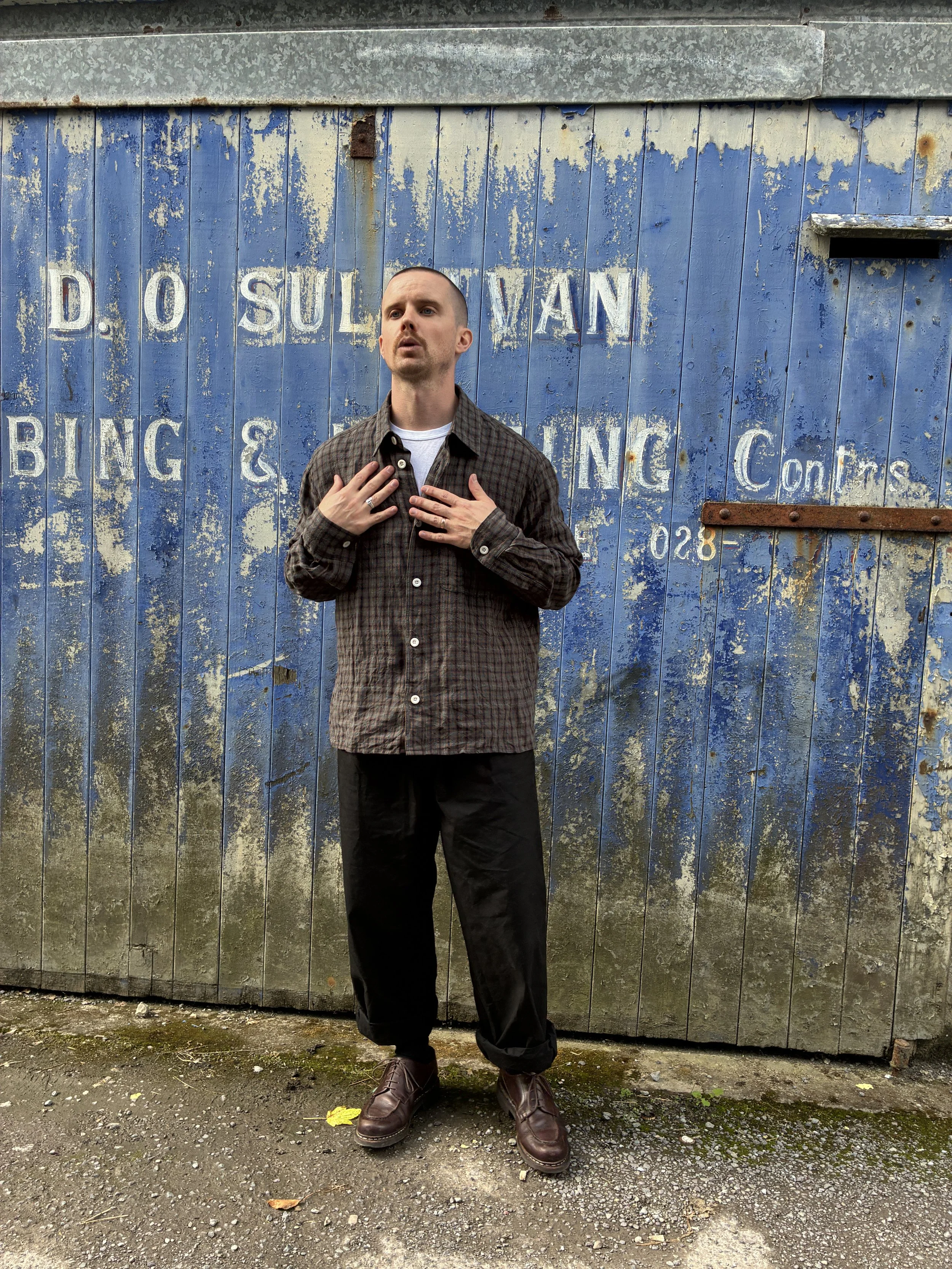 Man wearing Dusk Conkers Relaxed Farmer Shirt in front of rusty blue shutter