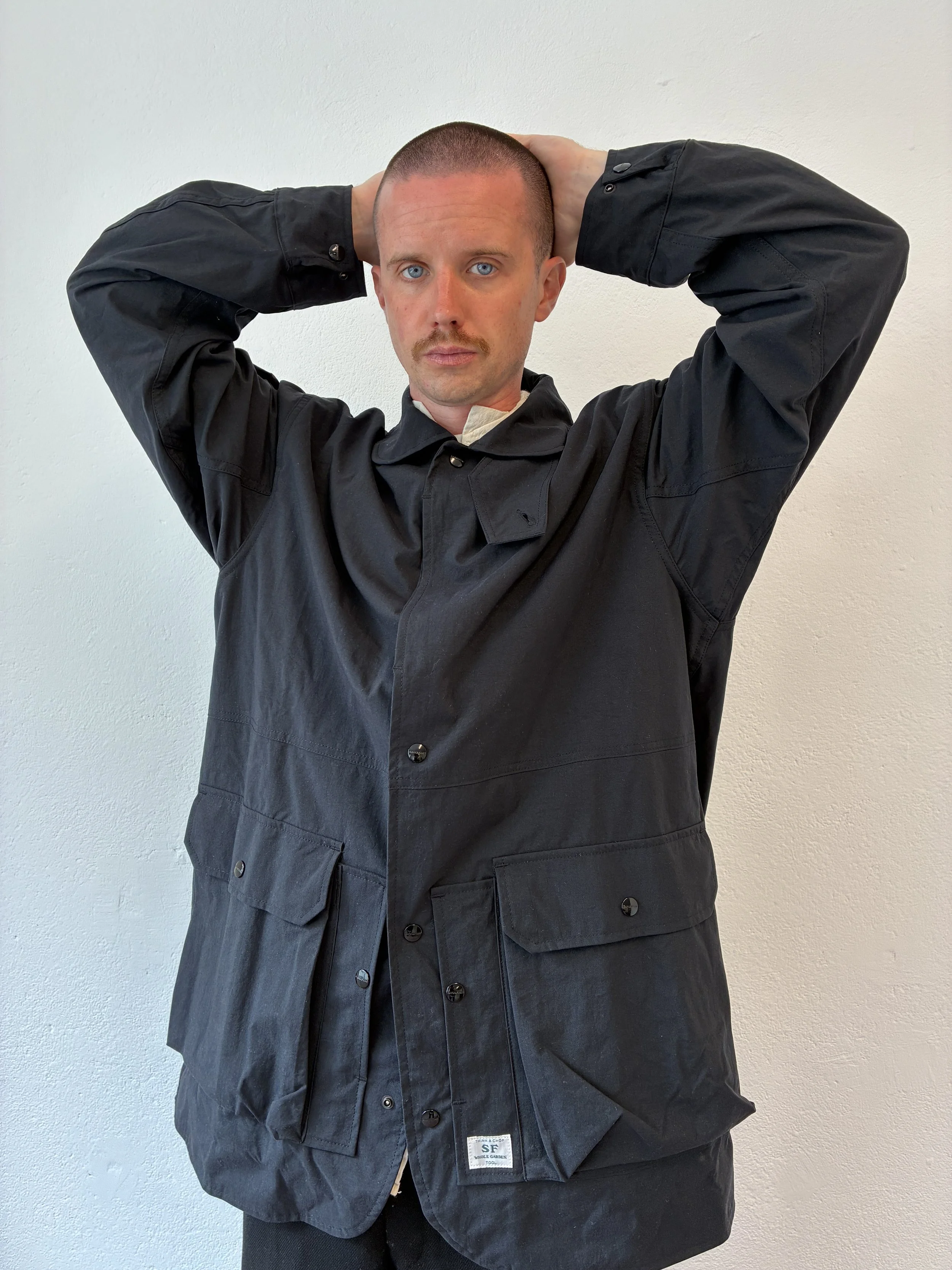Man posing with hands on head while wearing Black Sassafras Cultivator Coat