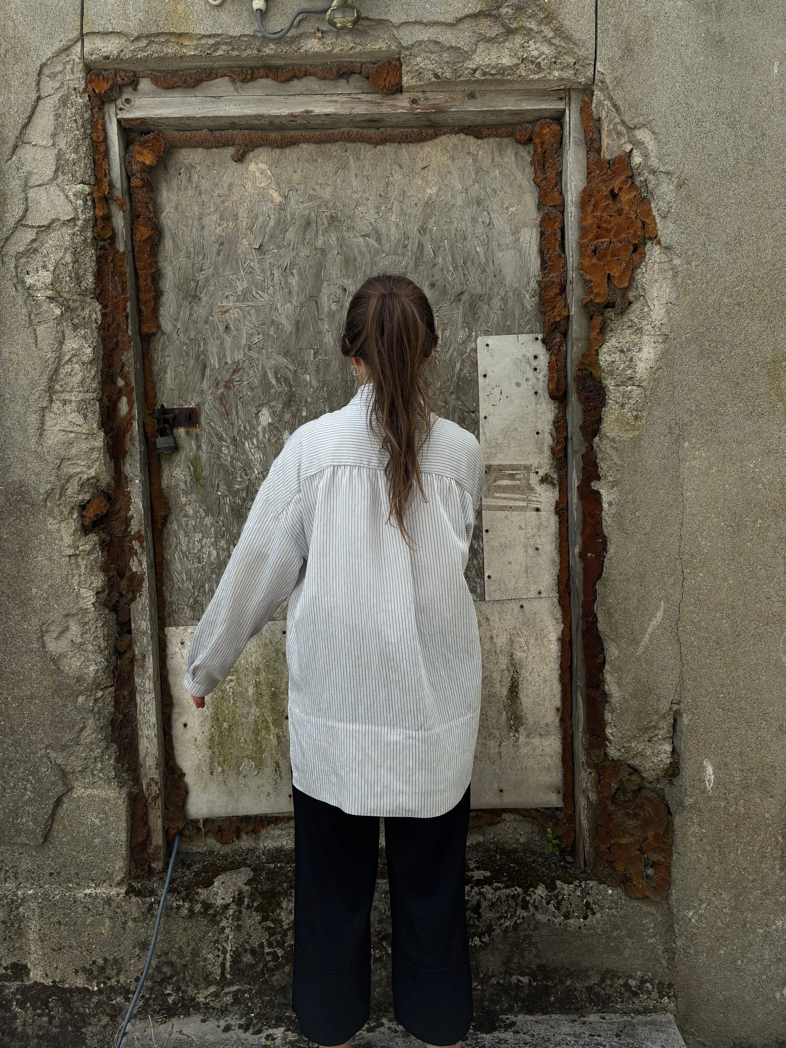 Back of woman in front of wall wearing 1st PAT-RN Woman Modula Shirt in Fine Stripes
