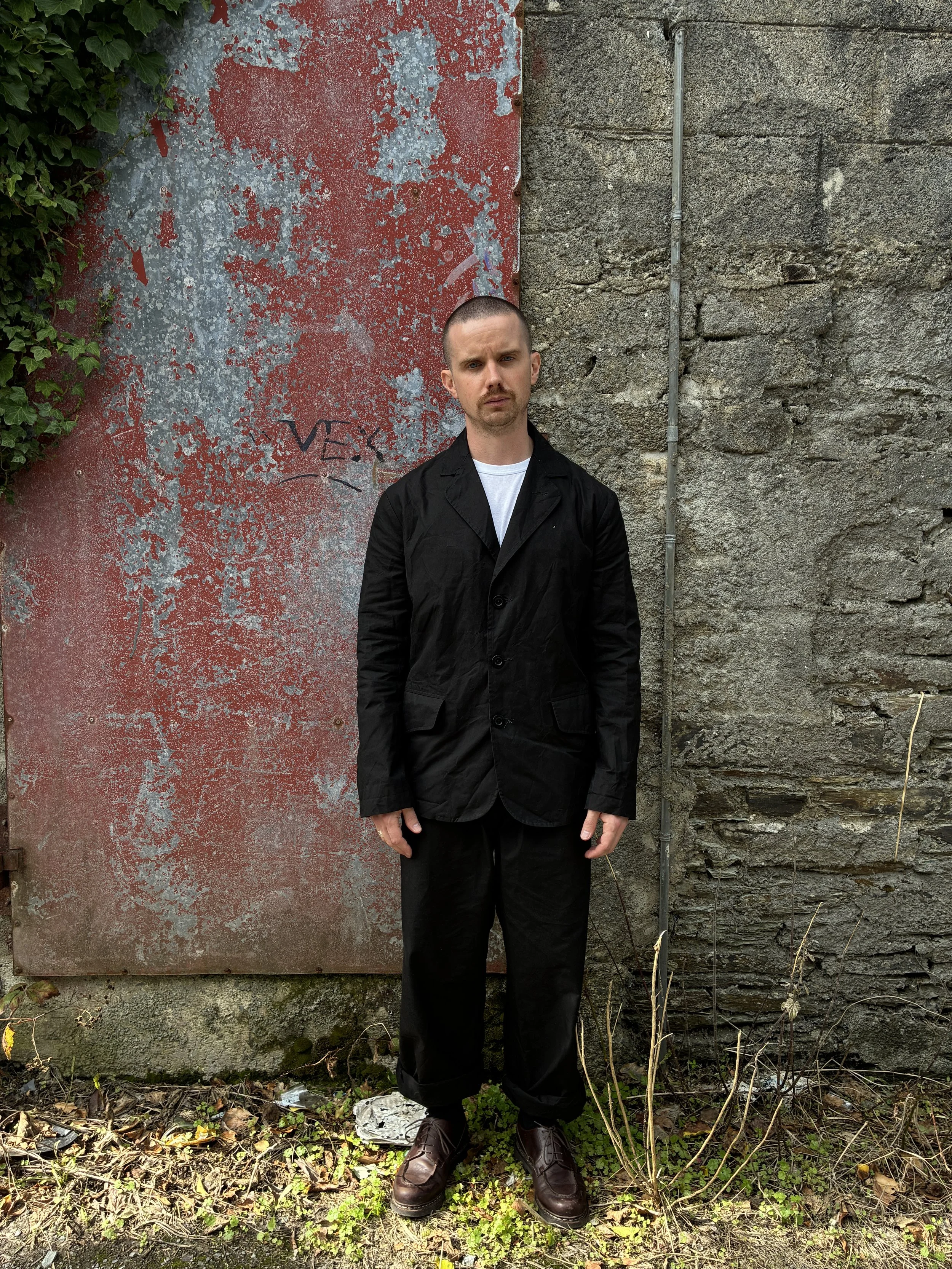 Man in front of red wall outside wearing Black Conkers Rambler Blazer and trousers
