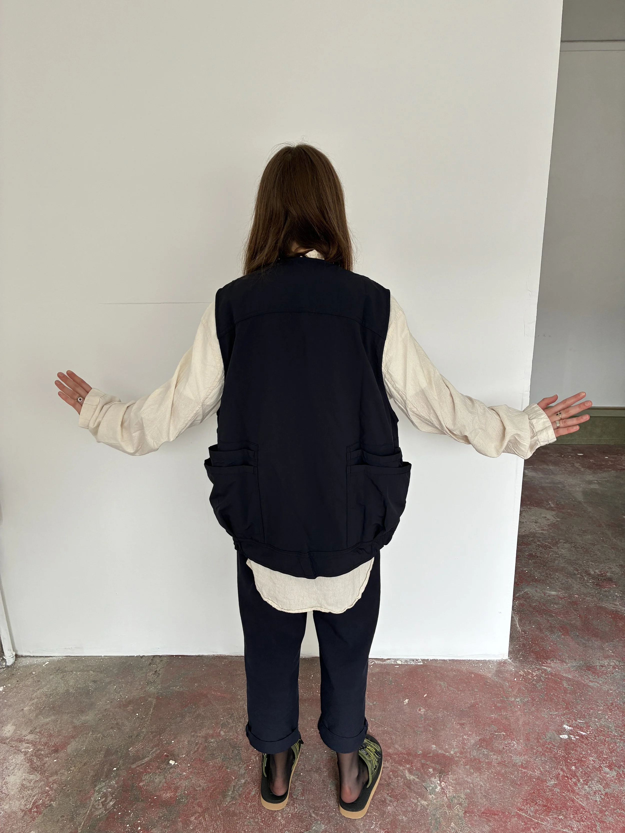 Back of Woman wearing Navy Sassafras Overgrown Hiker Vest in front of concrete wall