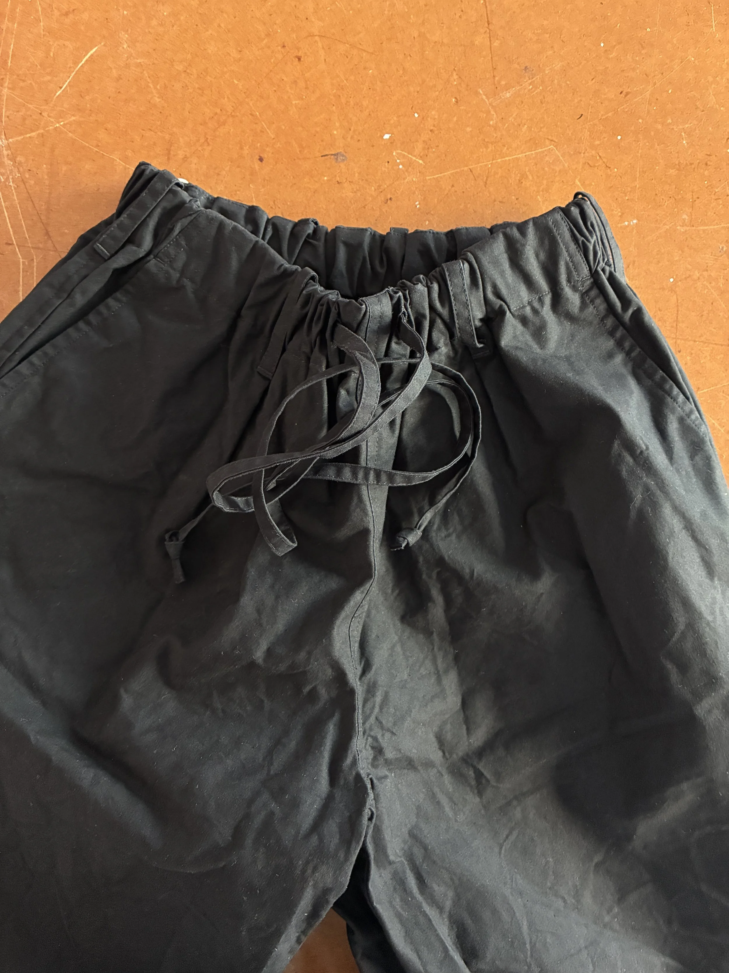 Waist of Conkers Rambler Black Waxed Cotton Trousers folded on brown table