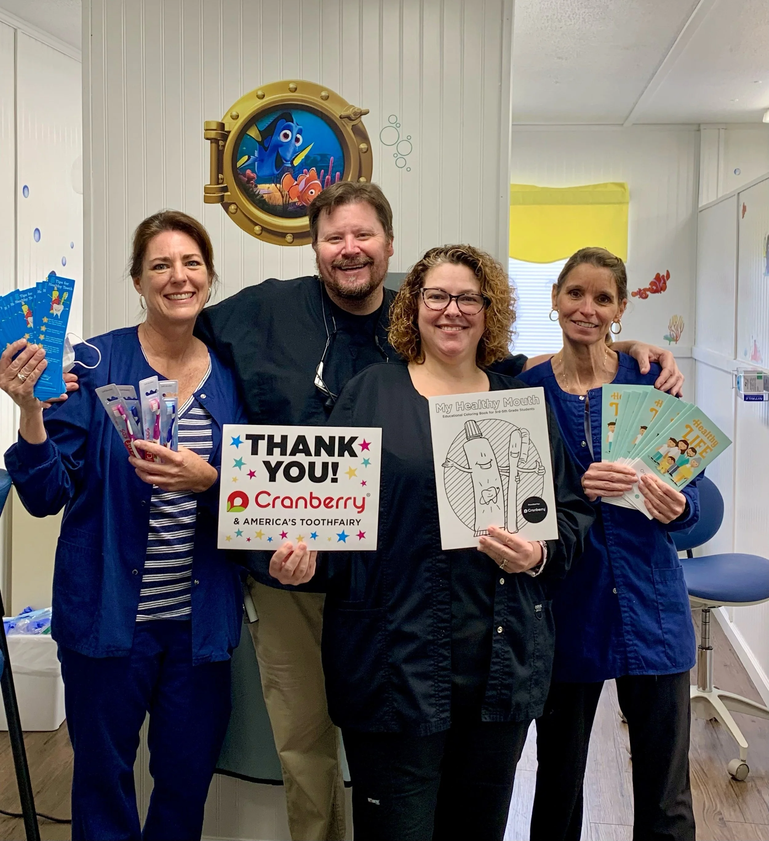 Four people smiling, holding dental products and a thank you sign in a dental office.