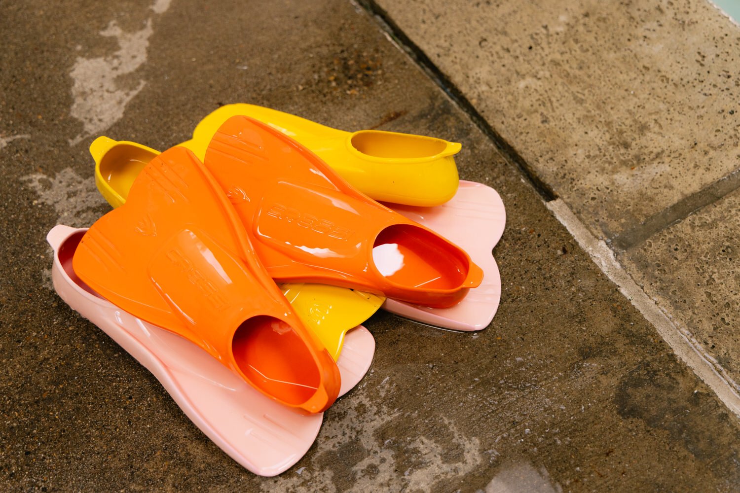 A pair of pink, yellow, and orange rubber slippers lying on a wet concrete ground near a concrete step.
