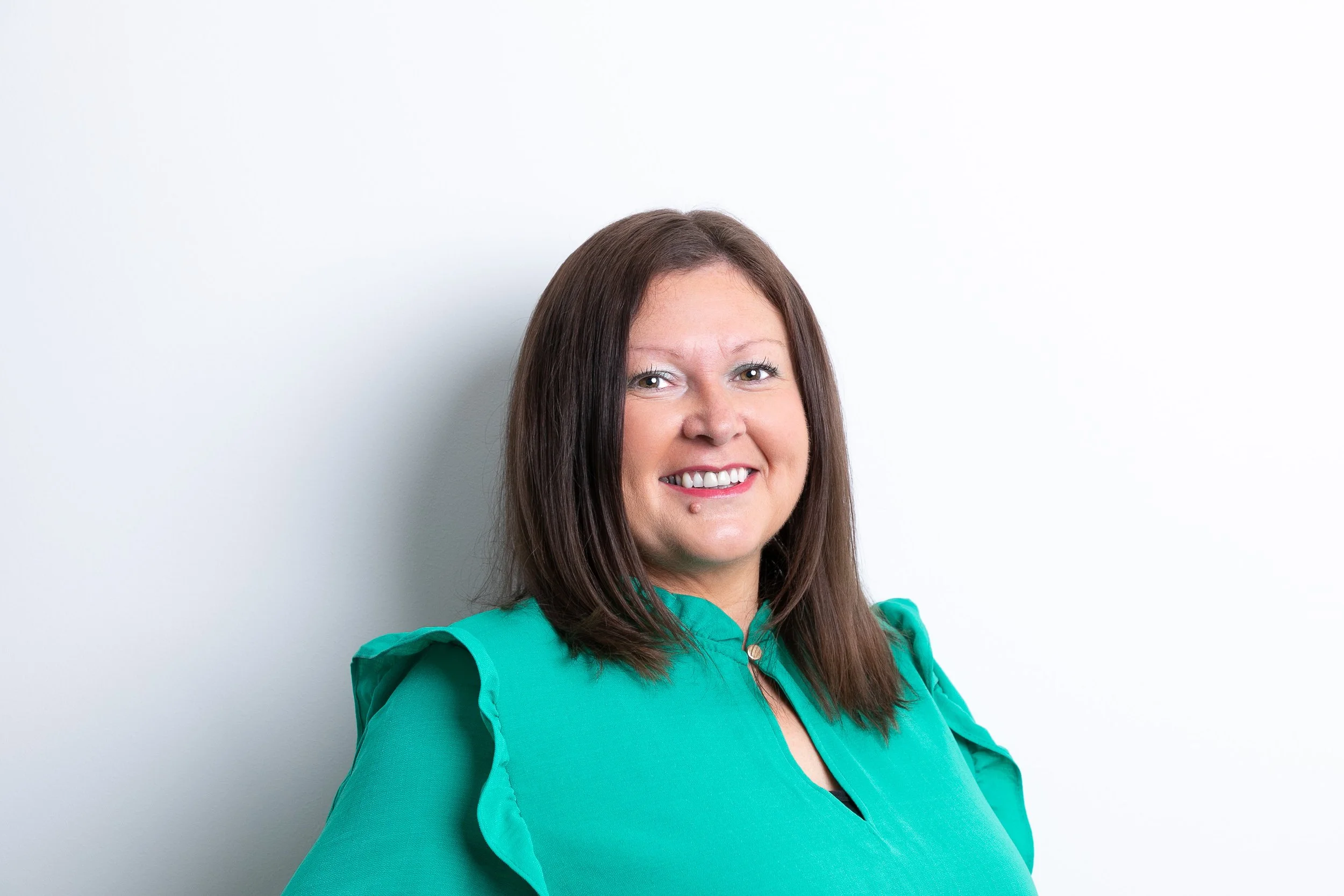 A woman with shoulder-length brown hair in a teal blouse smiling against a plain white background.
