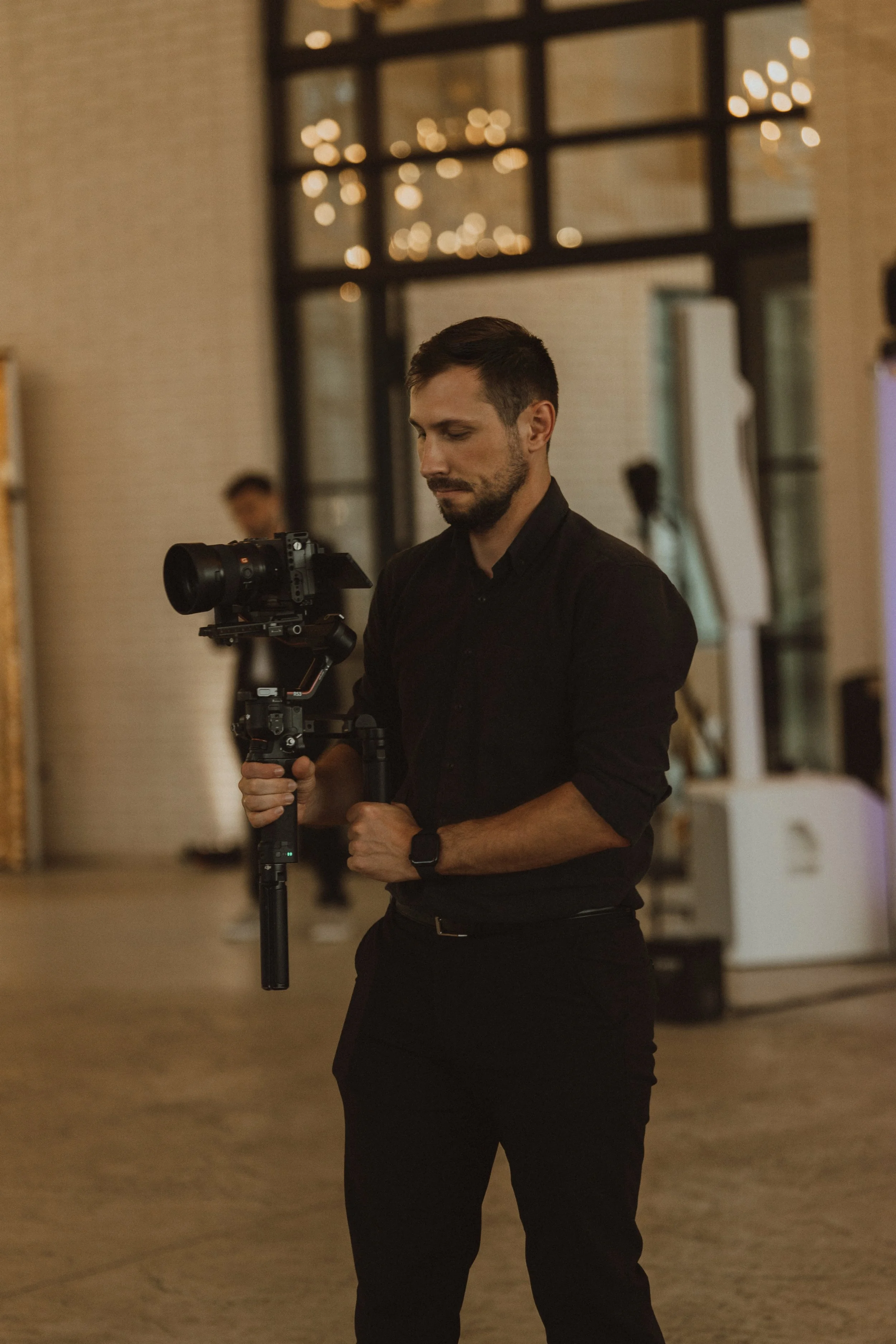 Wedding Videographer Cleveland Oleh Tiurkin in black shirt operating camera on tripod in an indoor wedding with warm lighting and a modern background.