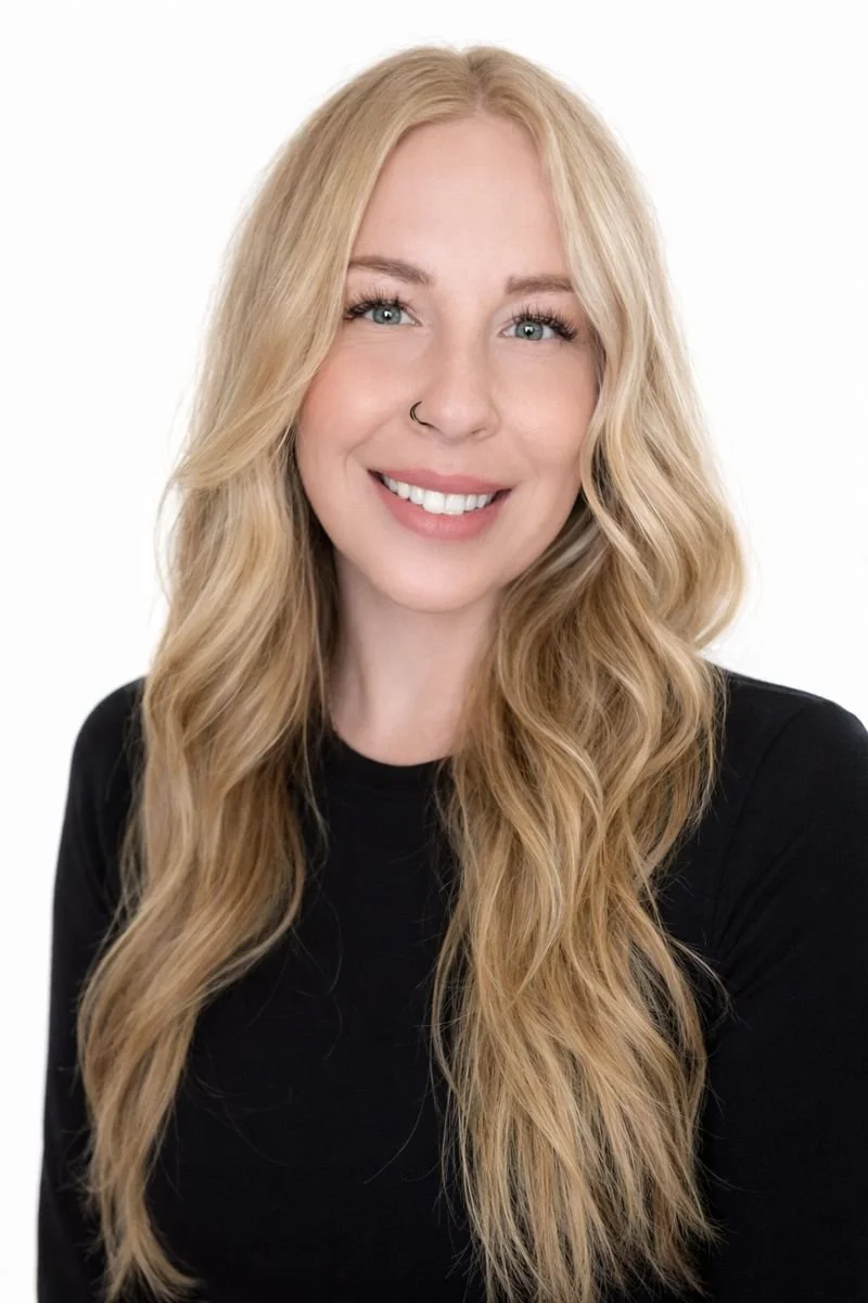 Smiling professional woman with long blonde hair in a black long-sleeve top on a white background.