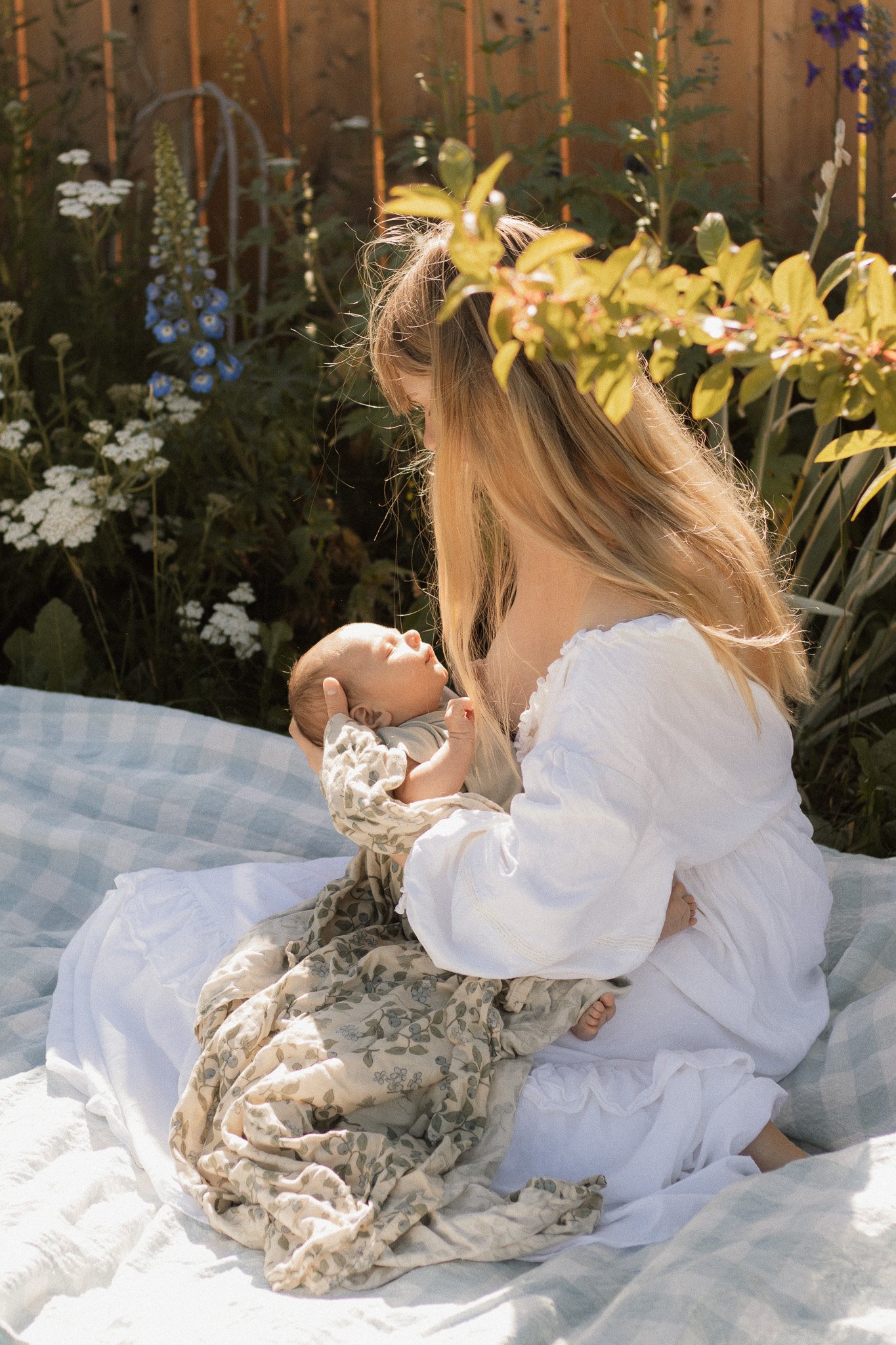 woman and newborn baby cuddle next to flower garden yarrow delphinium newborn photography golden bc