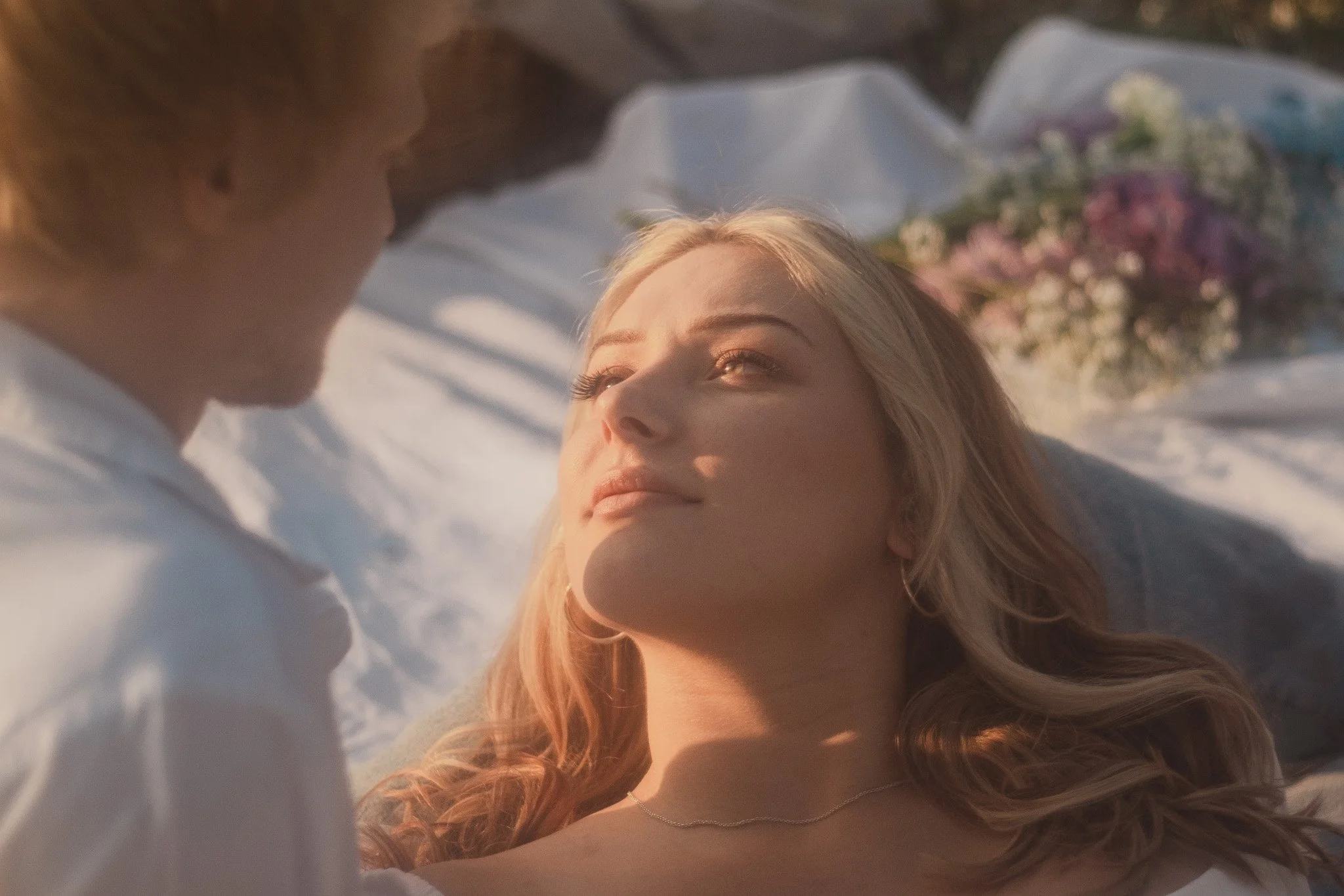 The golden hour sun illuminating face of beautiful expectant woman, her blond curls framing face as she looks up at her admiring husband.