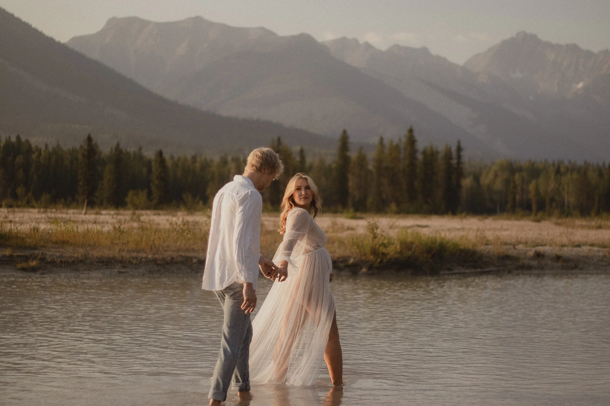 Maternity shoot in mountains of Golden, British Columbia at sunset. Golden hour illuminating the expecting couple.