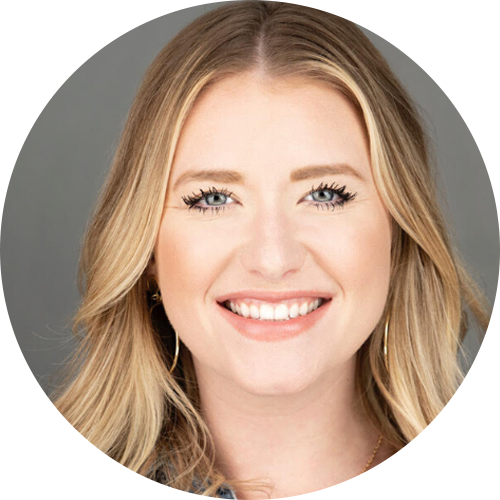 A smiling woman with blonde hair, blue eyes, and gold earrings, looking at the camera against a gray background.