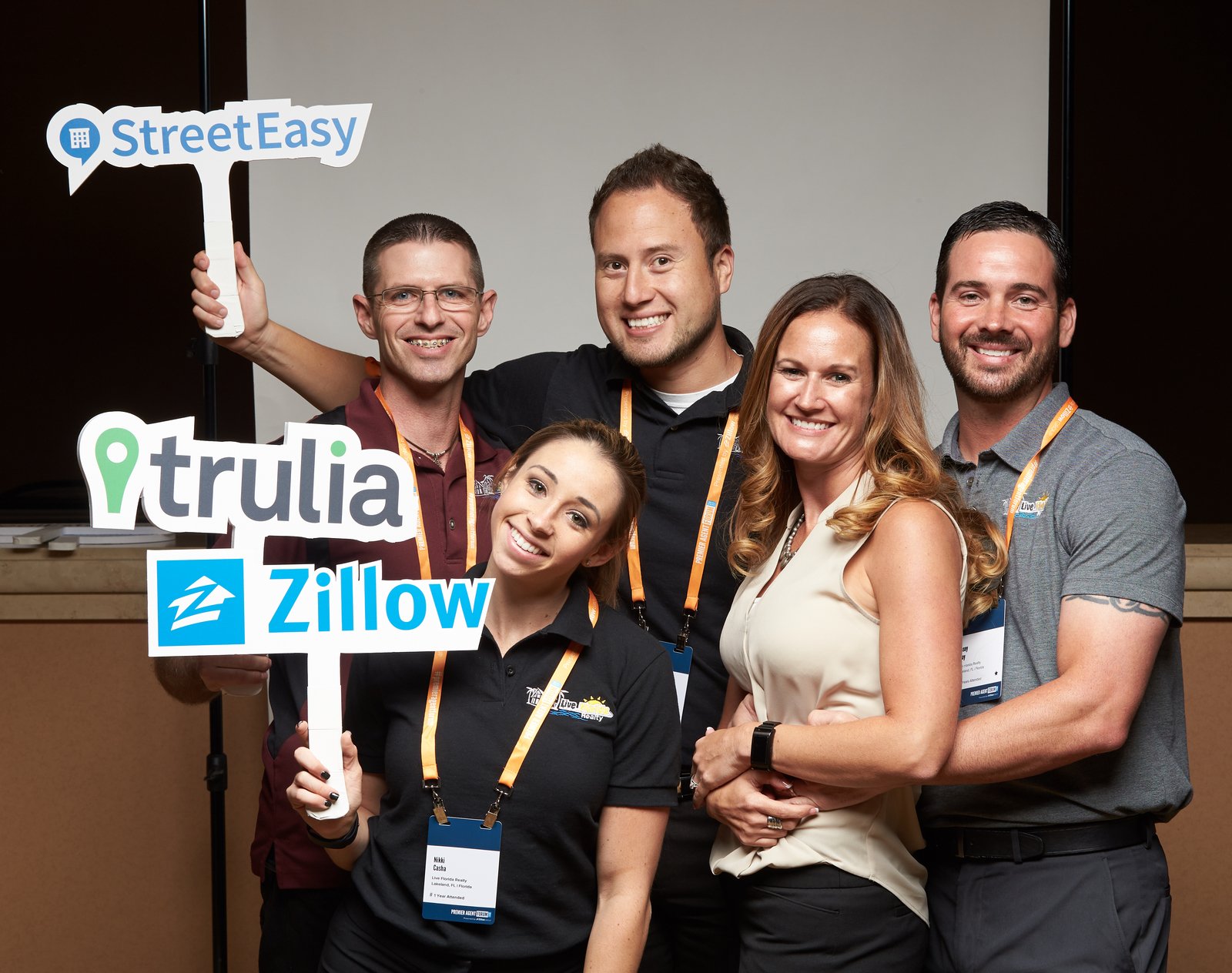 Group of six people smiling at a conference, holding signs for StreetEasy, Trulia, and Zillow. They are wearing conference badges and lanyards.