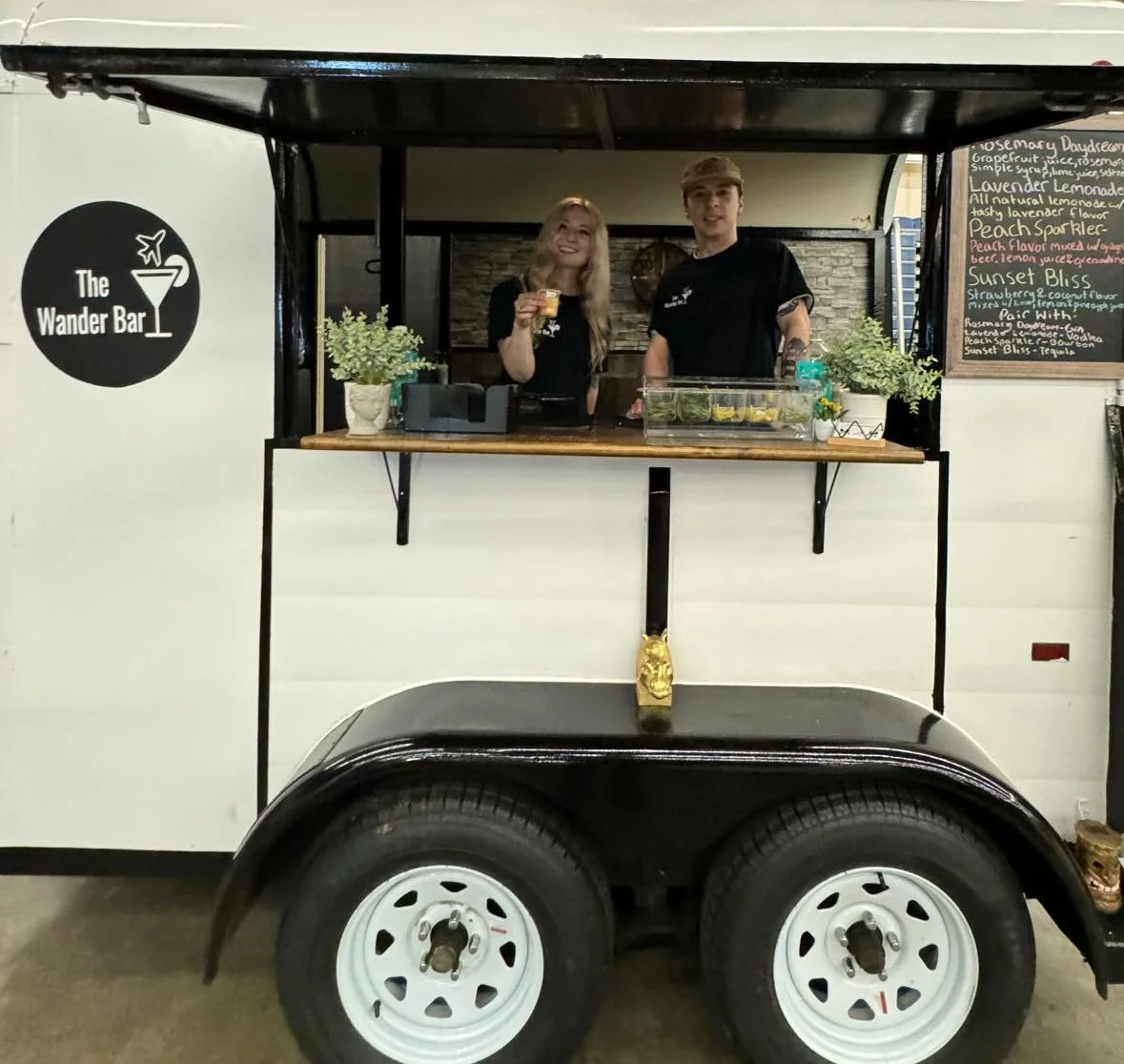Wedding bartenders Bridget and Rob smile as they hold up custom beverages that they are serving out of bar trailer at Shriner's bridal Show in Wilmington Massachusetts